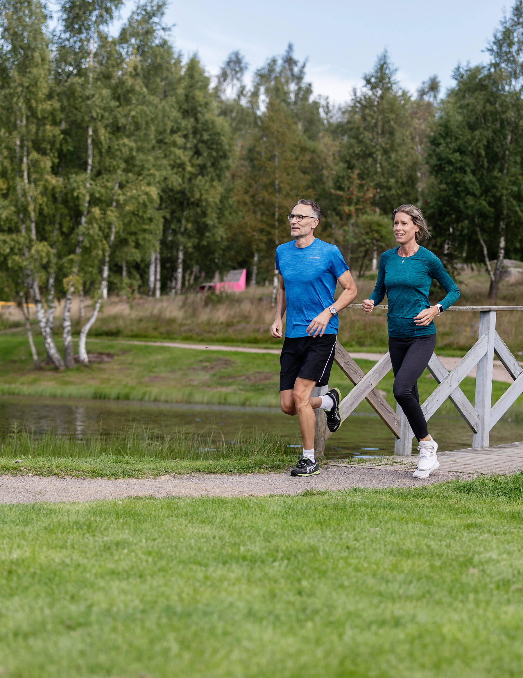 Kvinna och en man som springer över en träbro med vatten vid sidan.