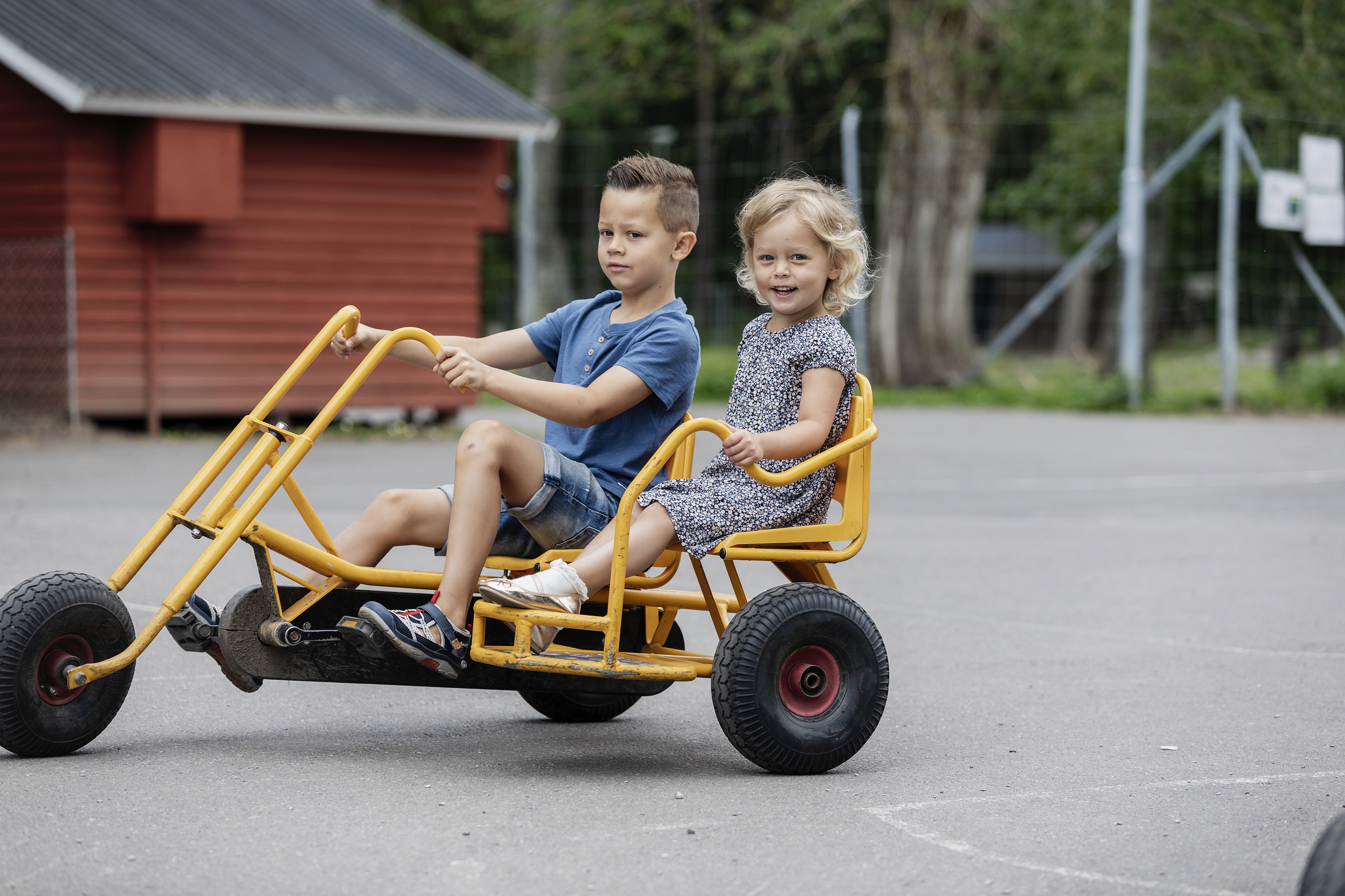 A boy and a girl ride a yellow pedal bike.