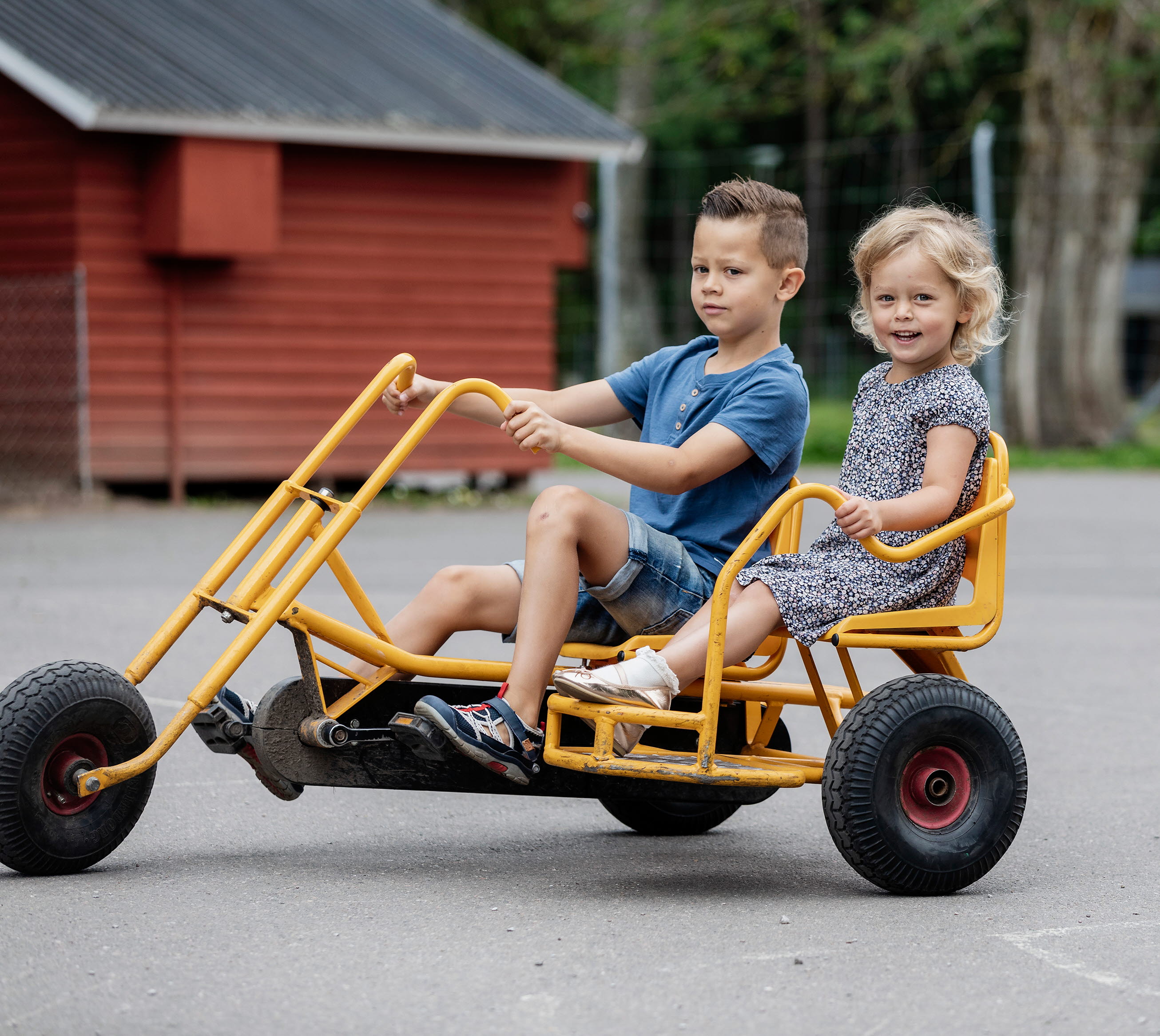 En pojke och en flicka åker på en gul trampcykel.