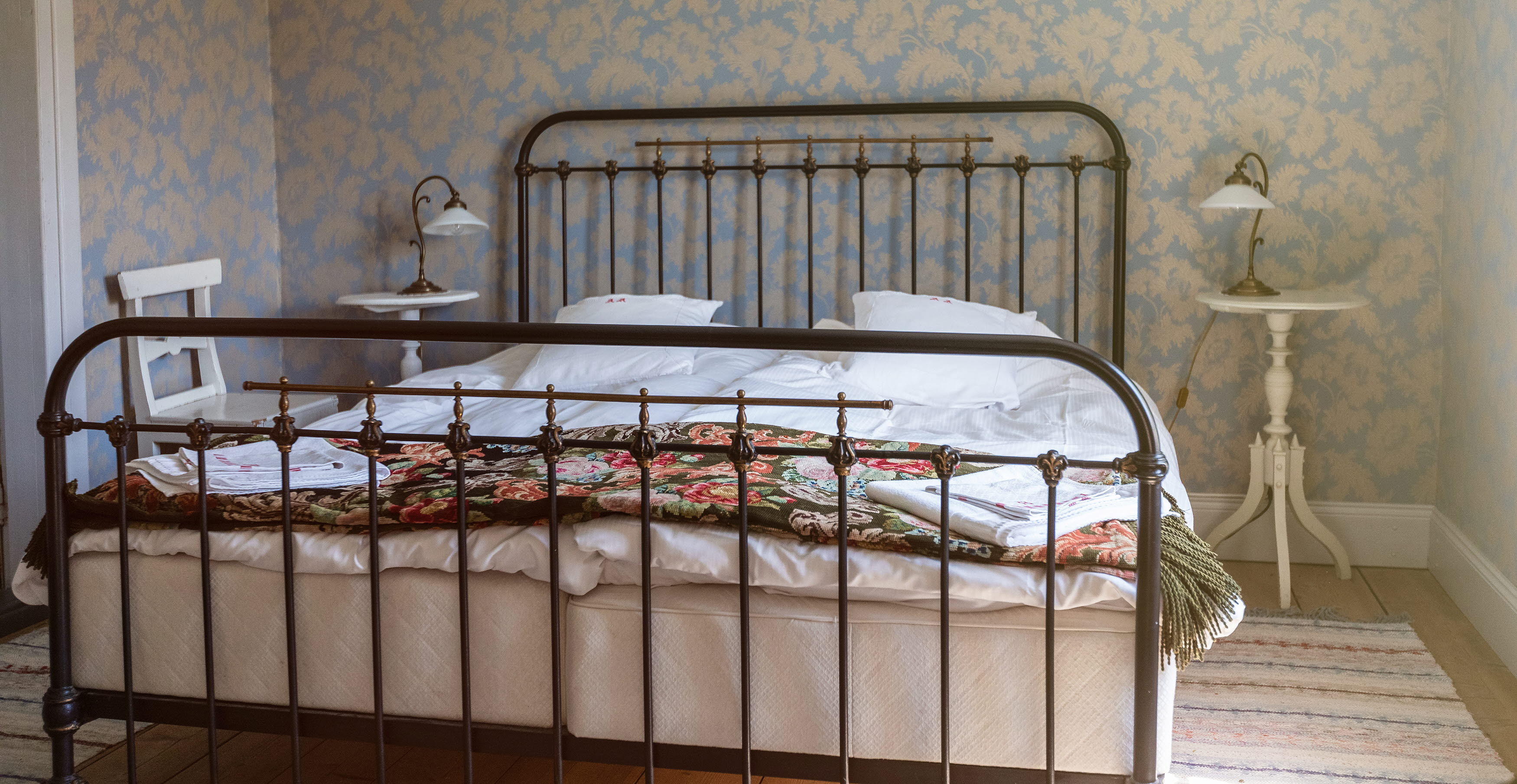 Double bed with iron frame, floral tapes in the background.