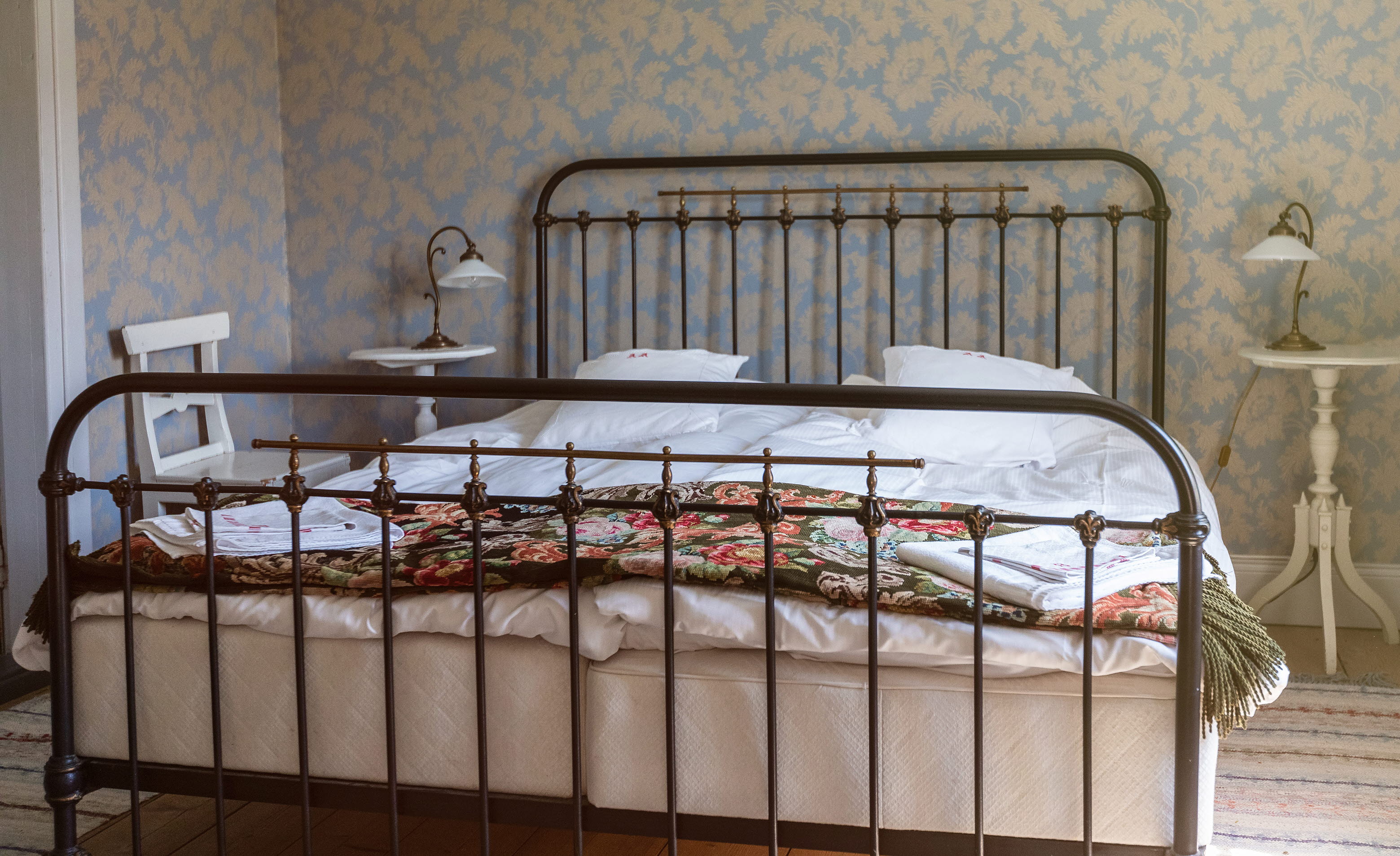 Dubbelsäng med järnram, blommiga taper i bakgrunden.