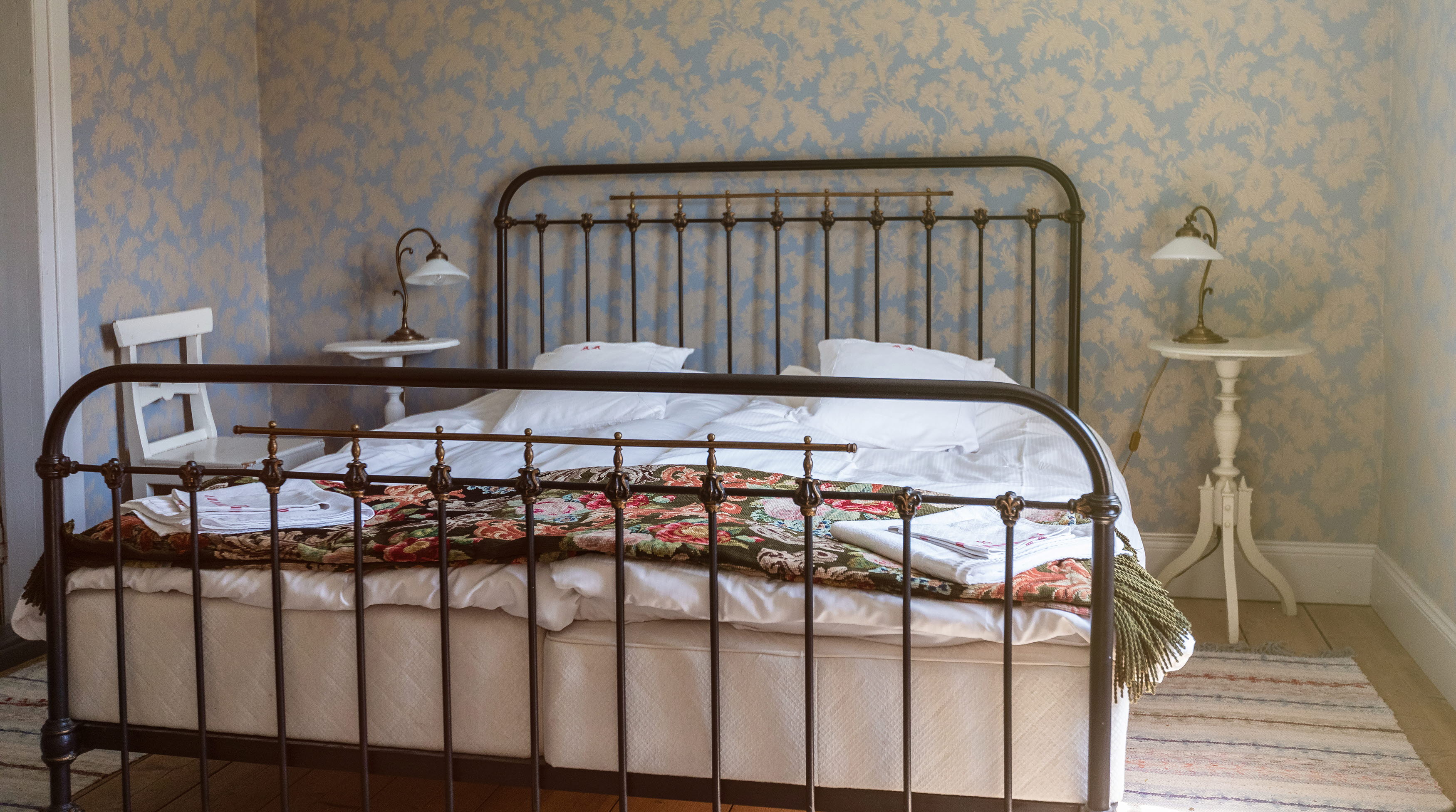 Dubbelsäng med järnram, blommiga taper i bakgrunden.