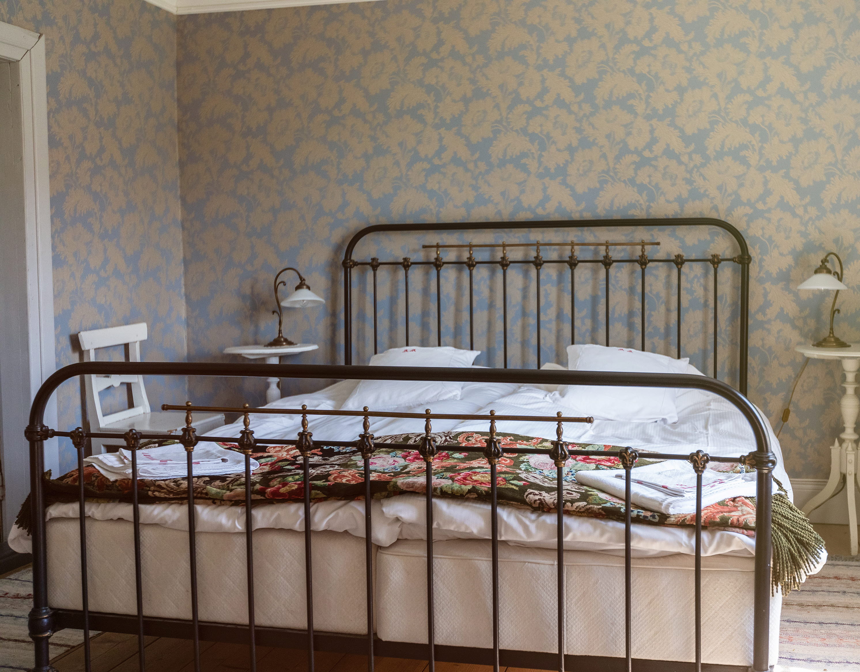 Dubbelsäng med järnram, blommiga taper i bakgrunden.