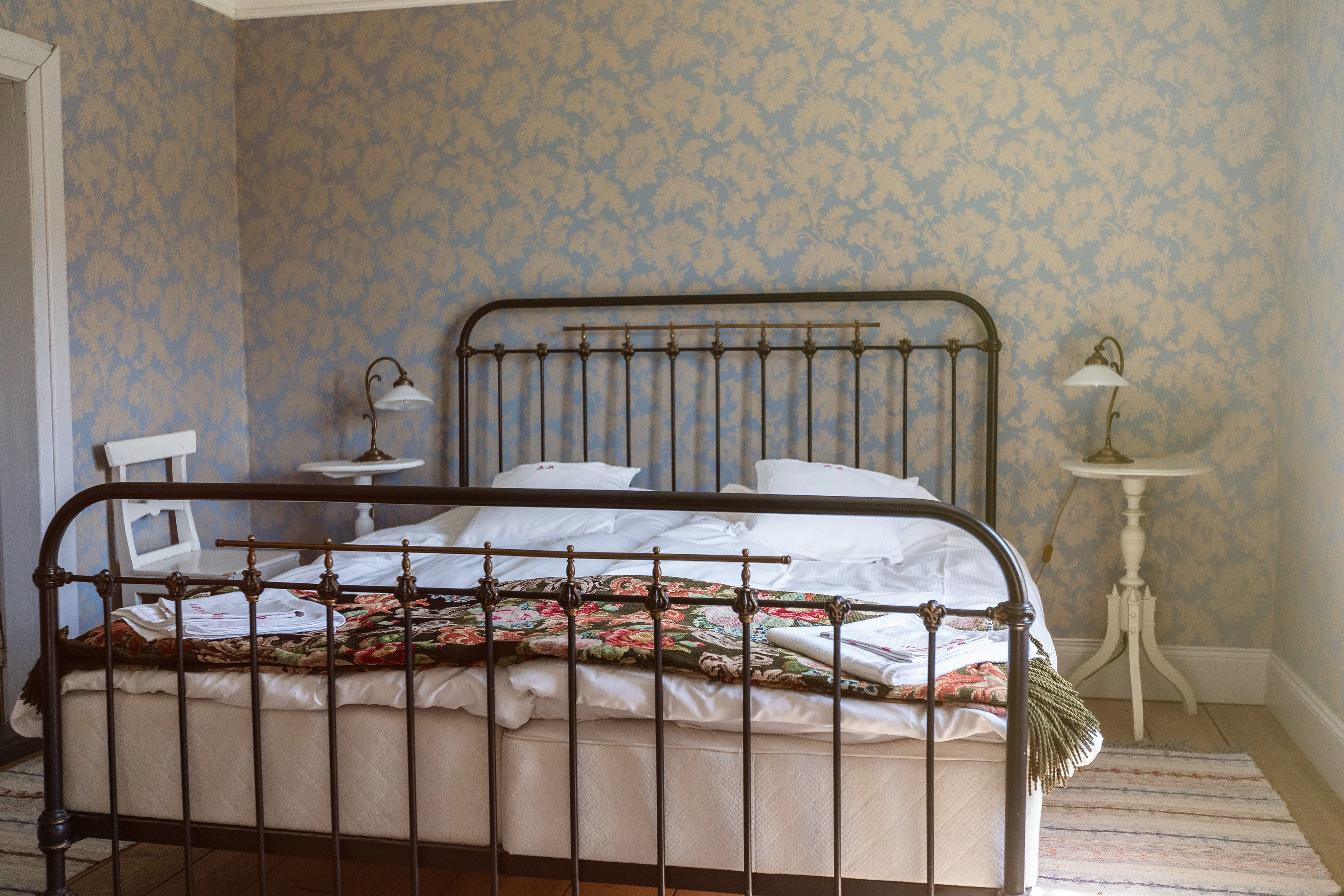 Double bed with iron frame, floral tapes in the background.