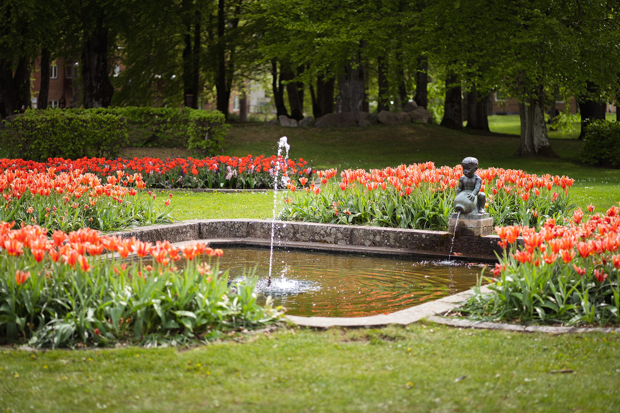 En bassäng i sten med en fontän. I kanten sitter en staty av en pojke som håller ett vattenkrus.