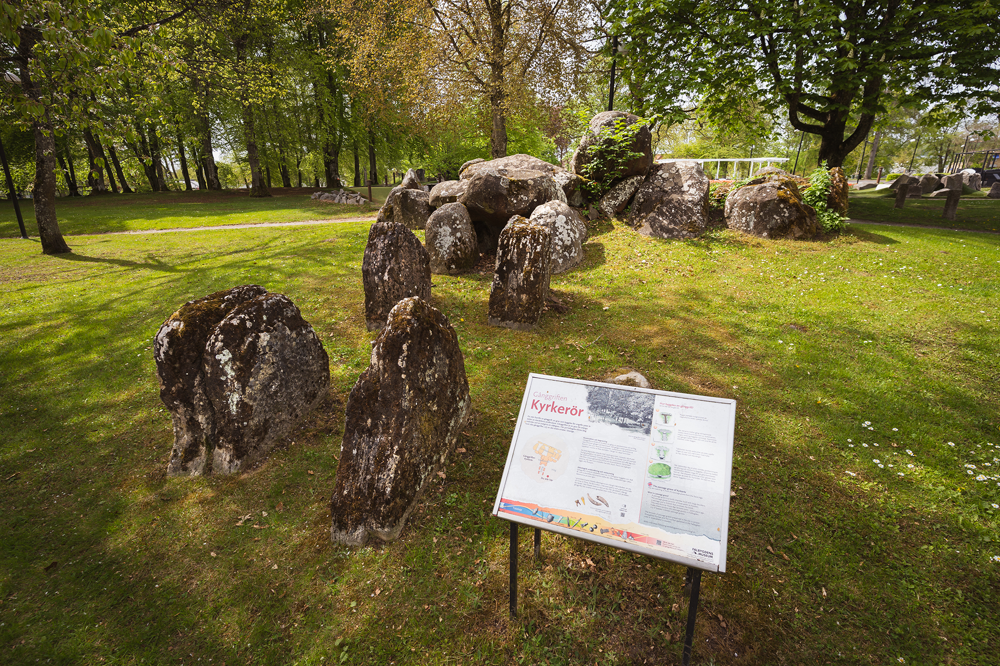Gånggift/megalitgrav i en park. Framför gånggiften sitter en skylt med information.