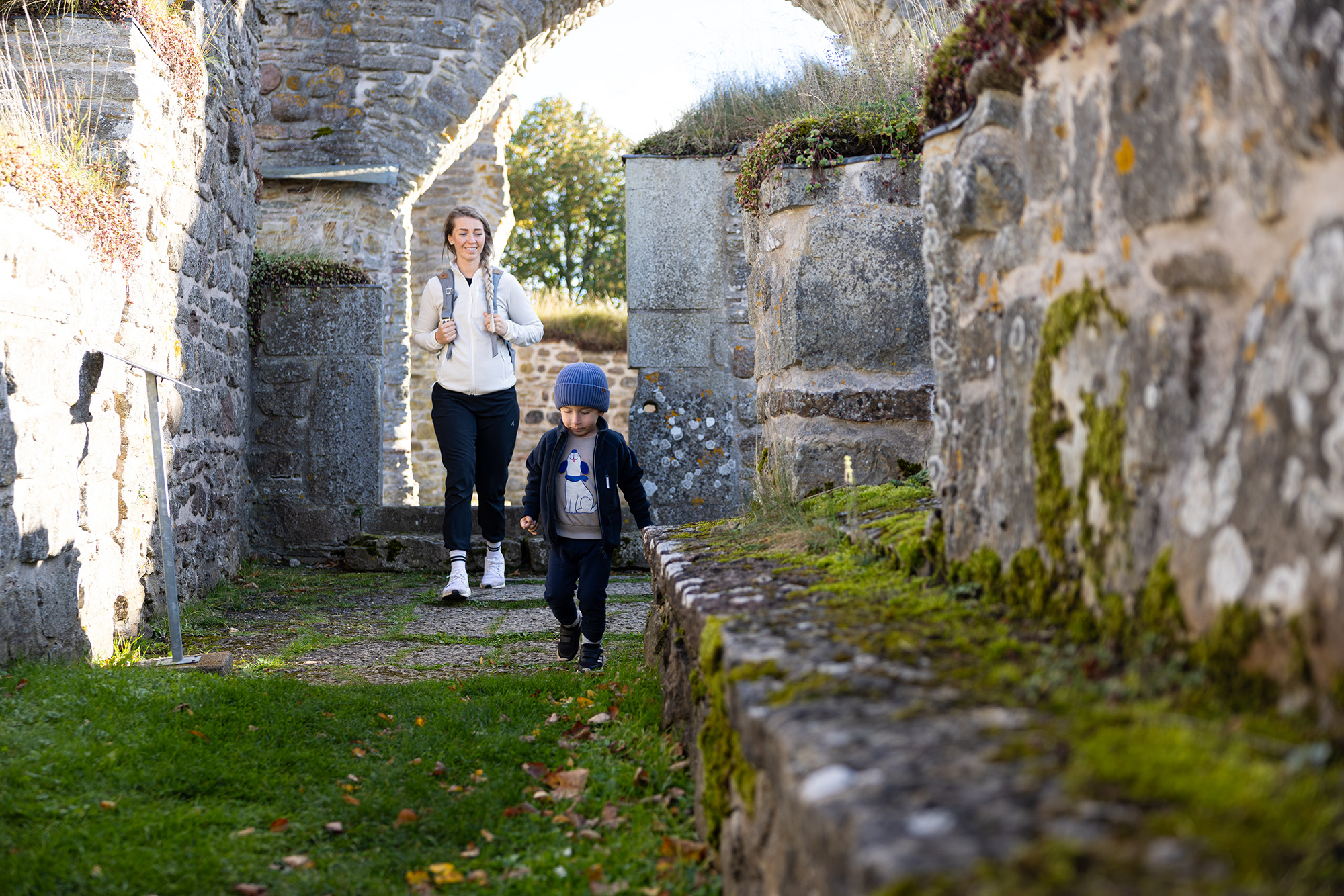 En kvinna och ett barn går i en klosterruin med stenväggar.