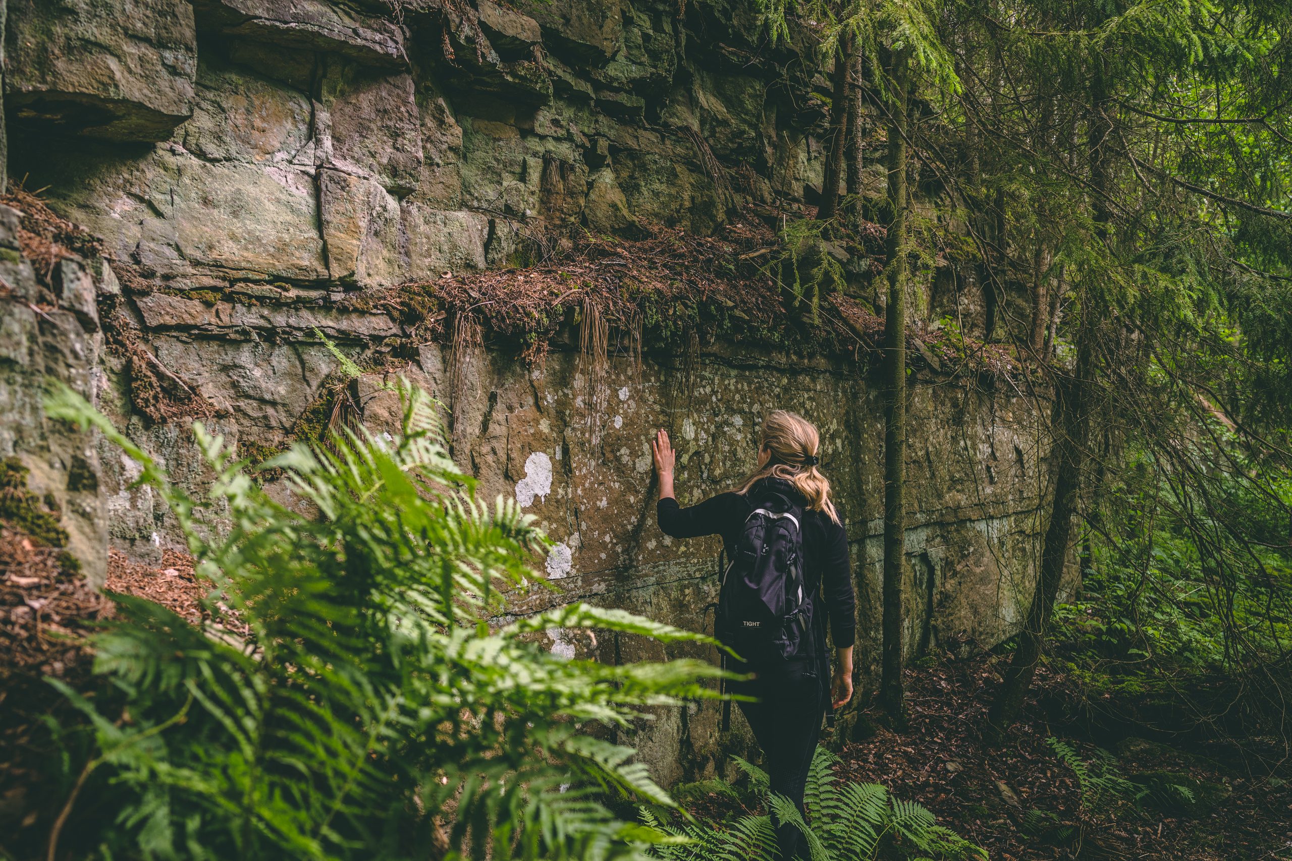 Woman standing by a mountain wall with her hand on the mountain.