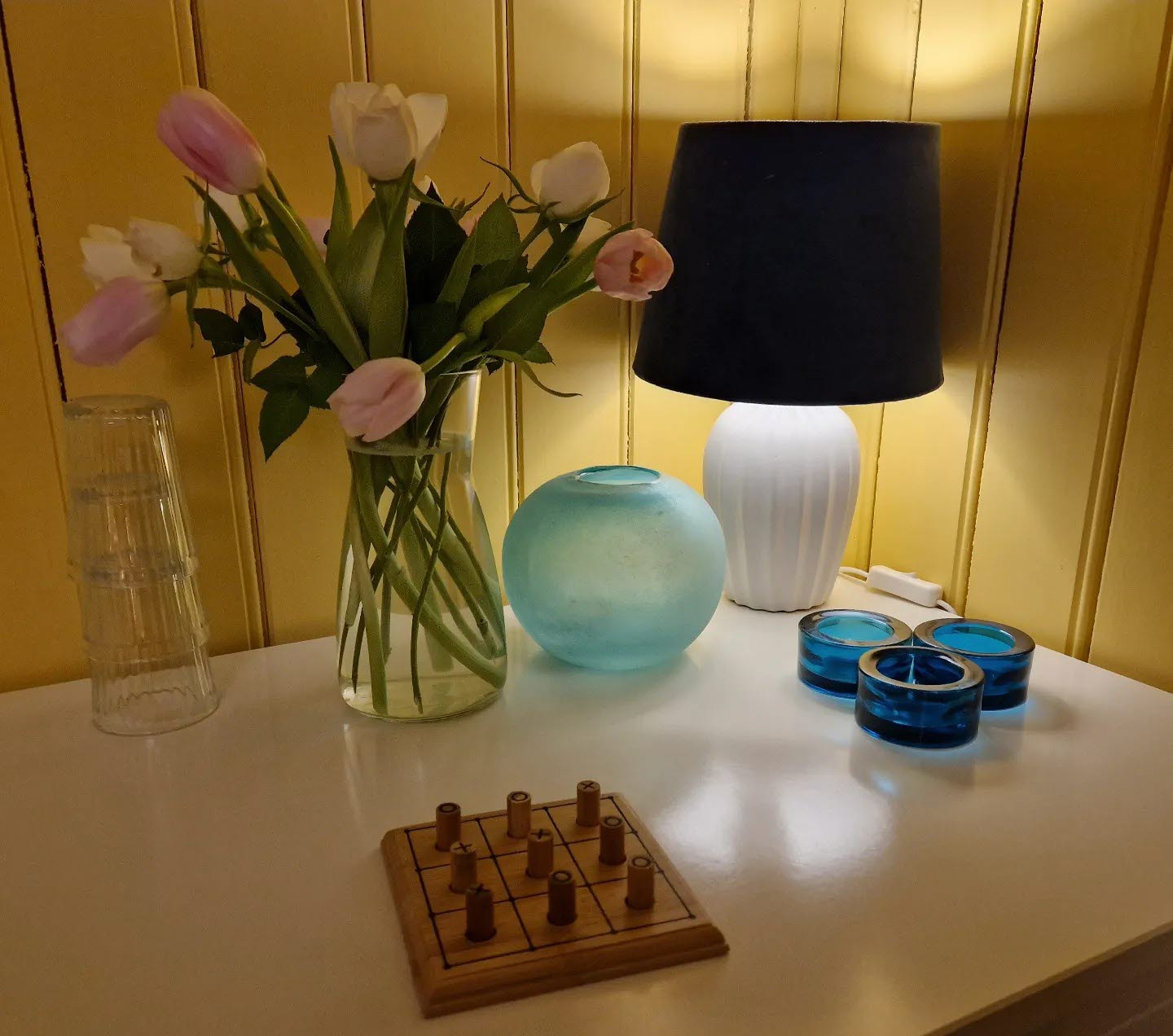 Ett vitt bord med en lampa, en vas med tulpaner och ett träspel.