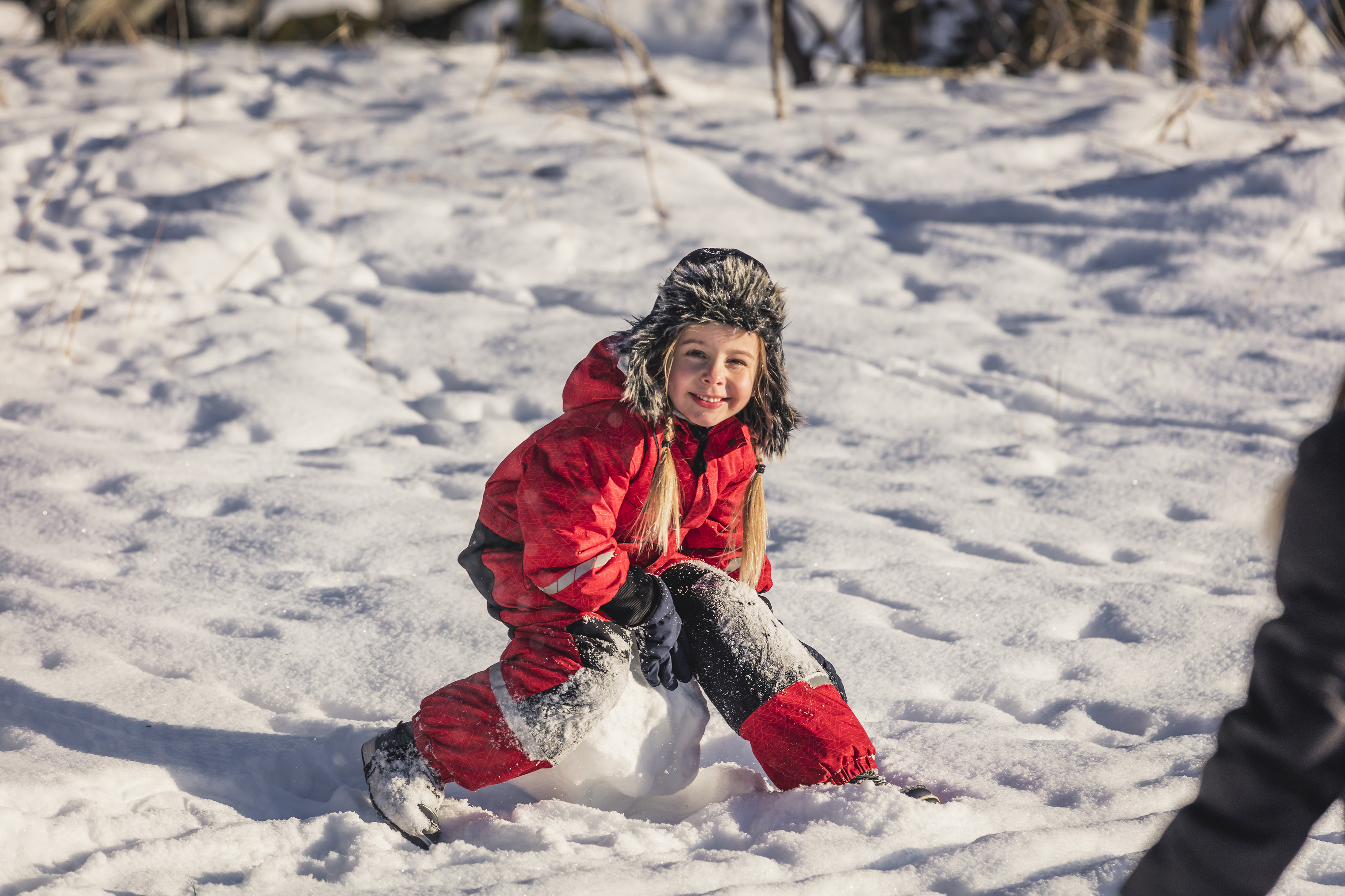 Flicka i röd overall som sitter på en stor snöboll.