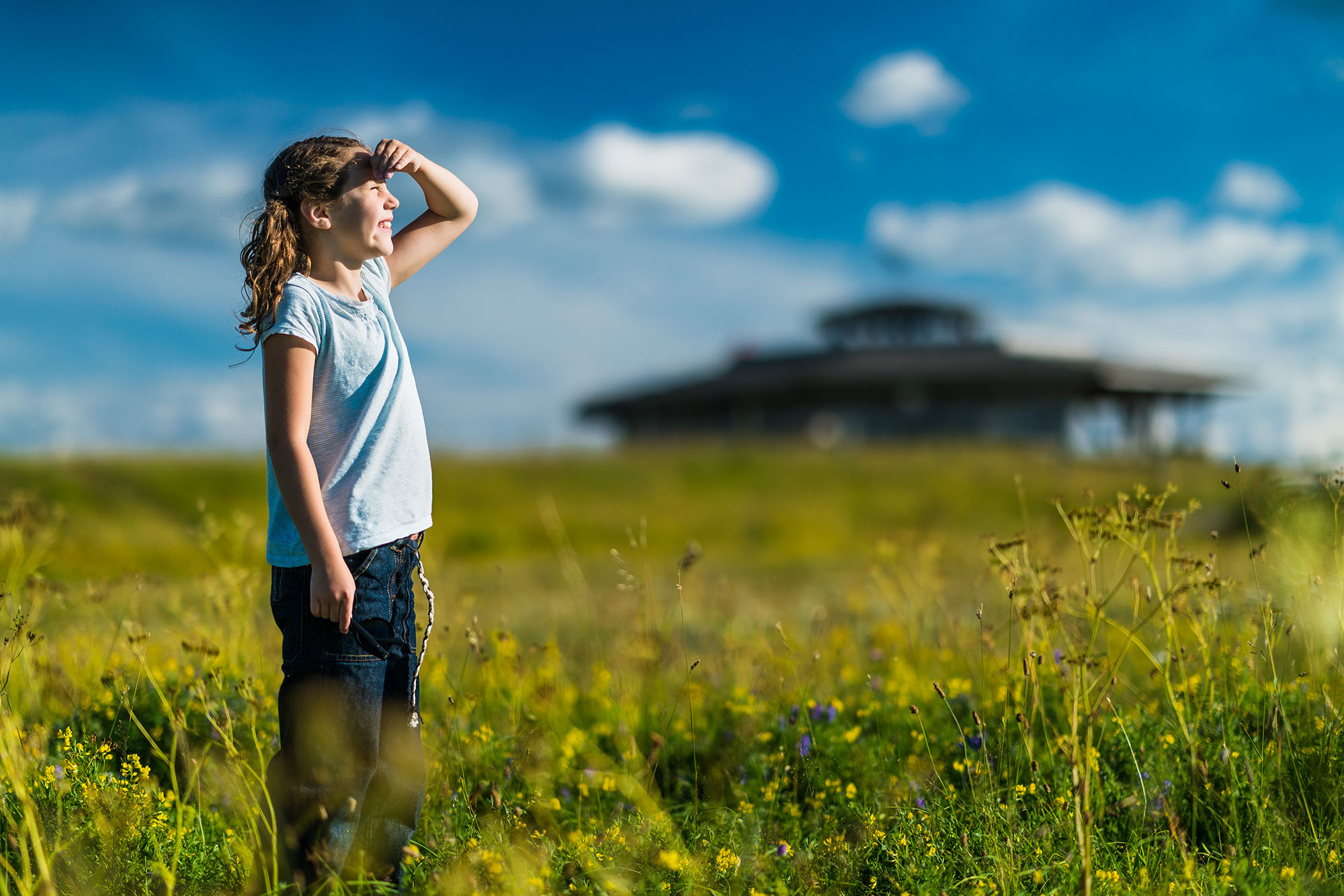 Flicka som står på en äng och kikar mot himlen. Utsiktstornet på Fågeludden är i bakgrunden.