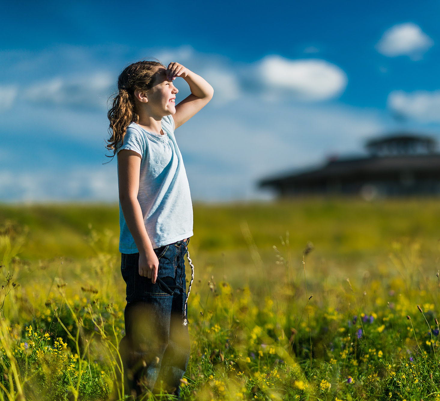 Flicka som står på en äng och kikar mot himlen. Utsiktstornet på Fågeludden är i bakgrunden.