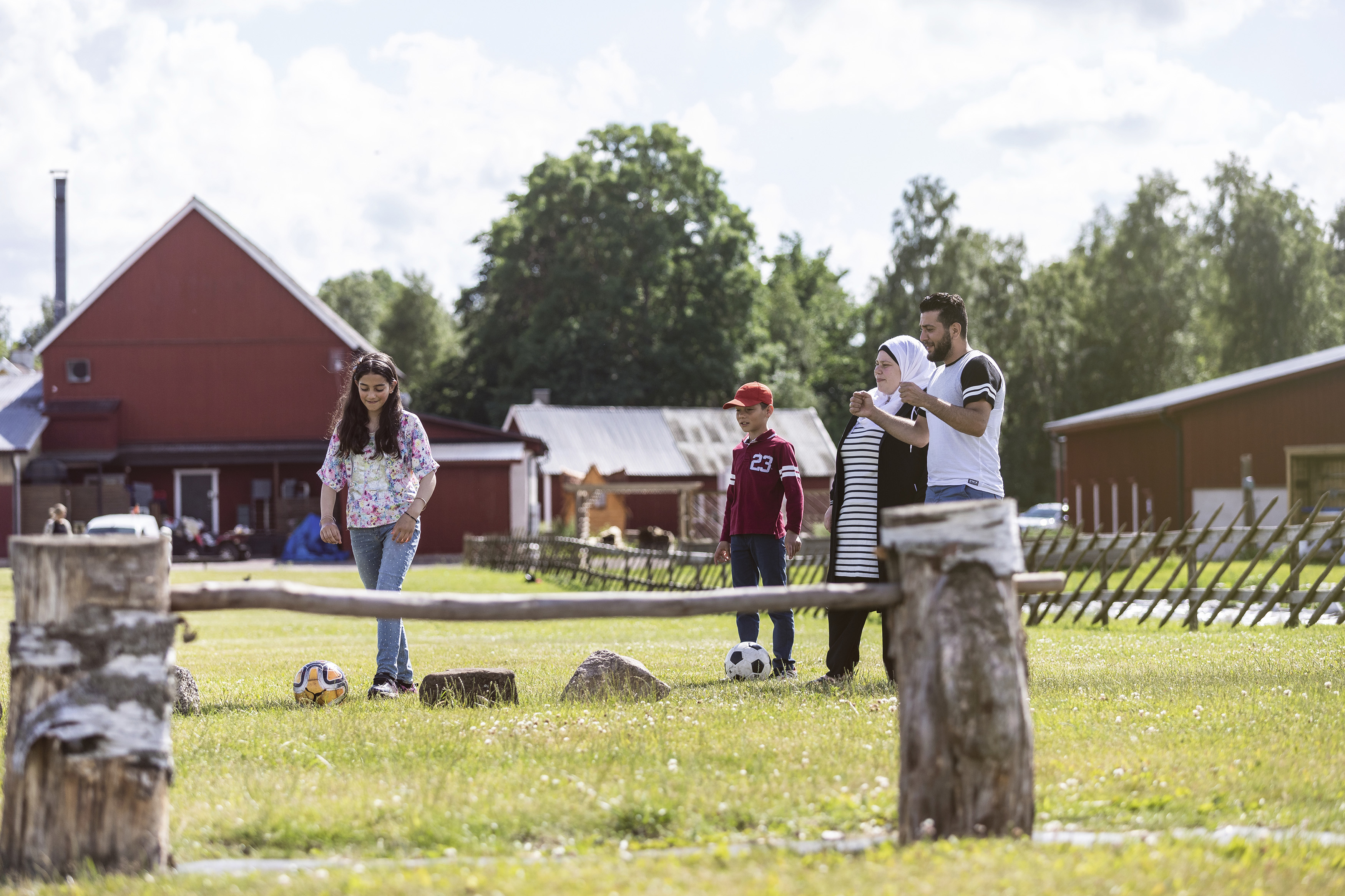 Flicka som sparkar fotboll över ett hinder. Familjen står vid sidan och hejar på.