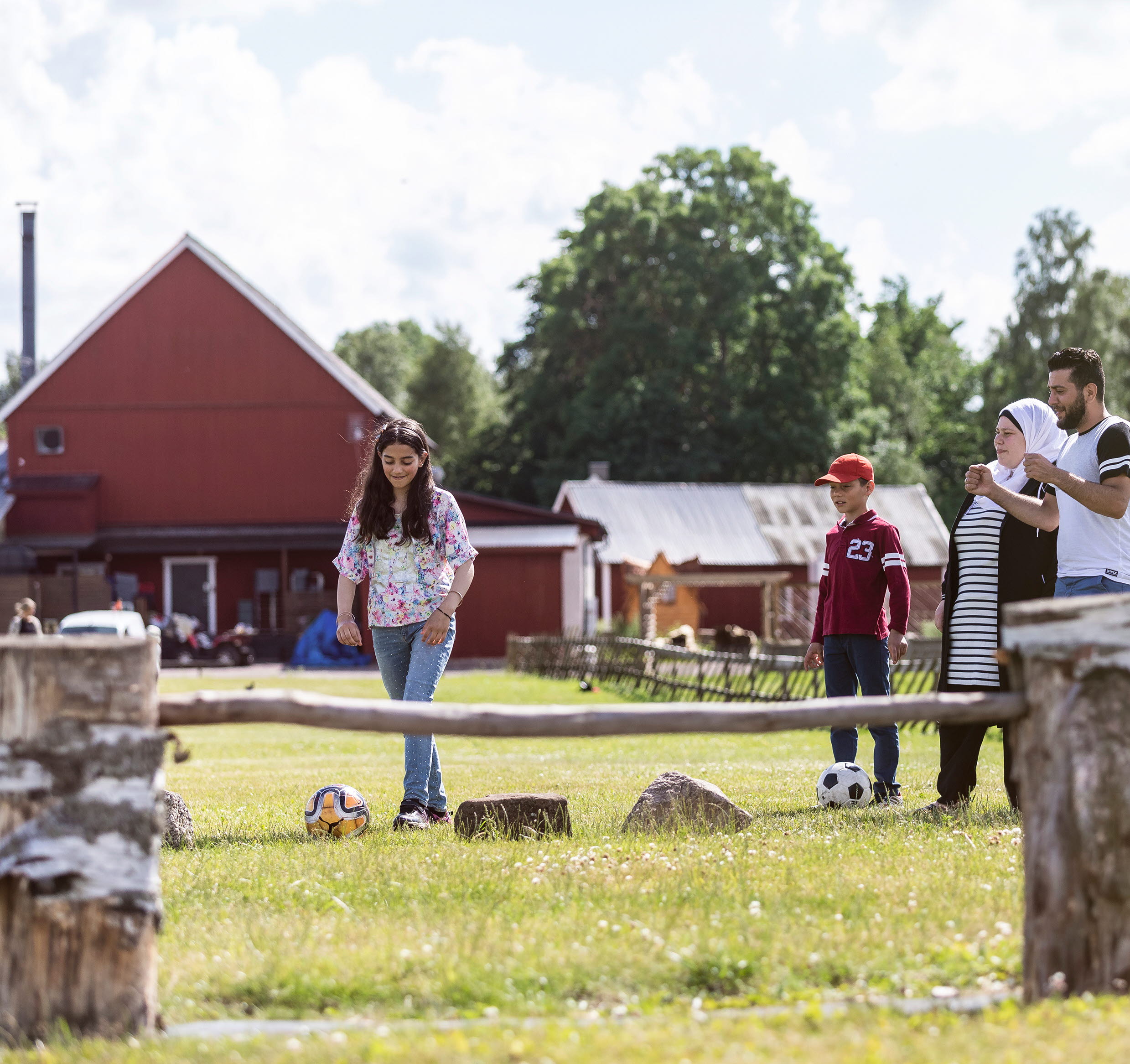 Flicka som sparkar fotboll över ett hinder. Familjen står vid sidan och hejar på.