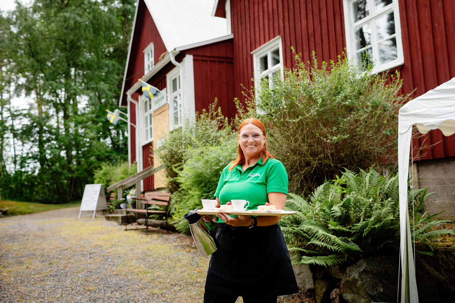 servitris håller upp bricka med våffla och kaffekopp utanför Skogshyddans kafé