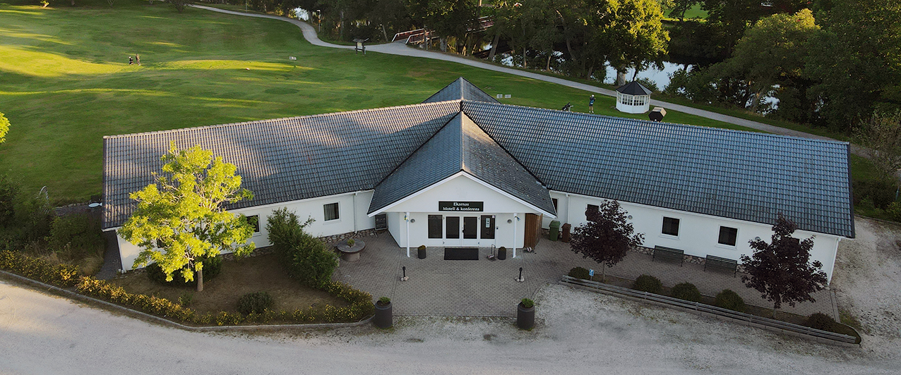 Drönarbild över Ekarnas motell och konferens. Bakom byggnaden syns golfbanan och Nossan som ligger blank. 