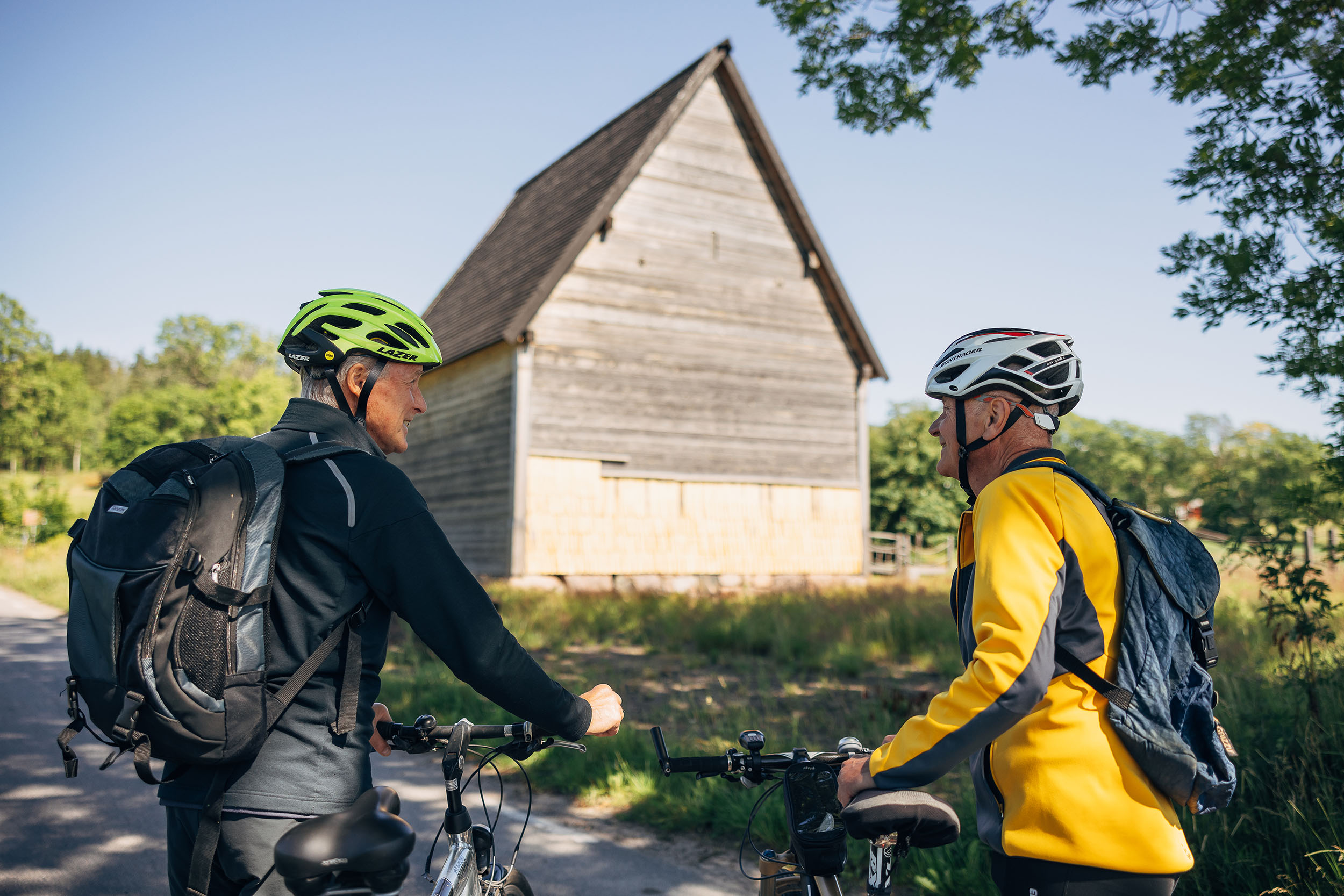 Två personer står bredvid sina cyklar. I bakgrunden syns Södra råda timmerkyrka. 