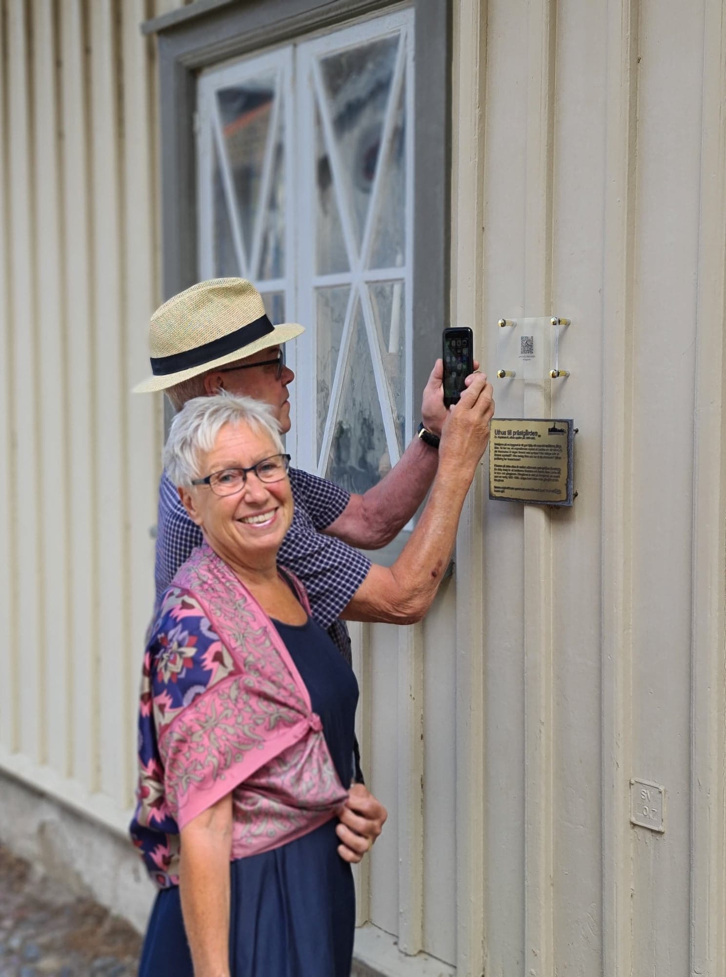 Par i Hjos trästad som scannar qr-kod vid en skylt. 