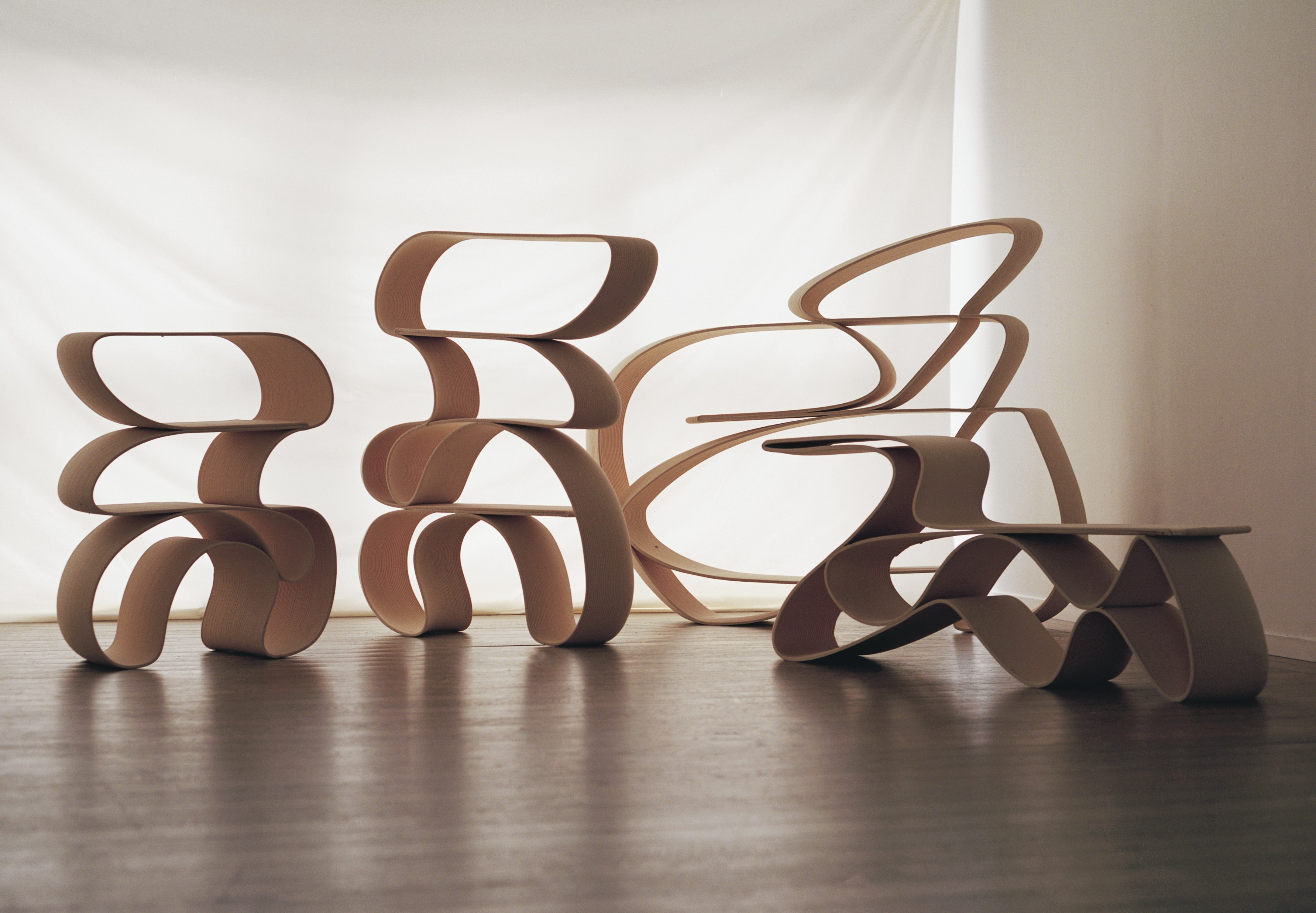 Several different furniture pieces with wavy shapes are positioned in a studio with a white background