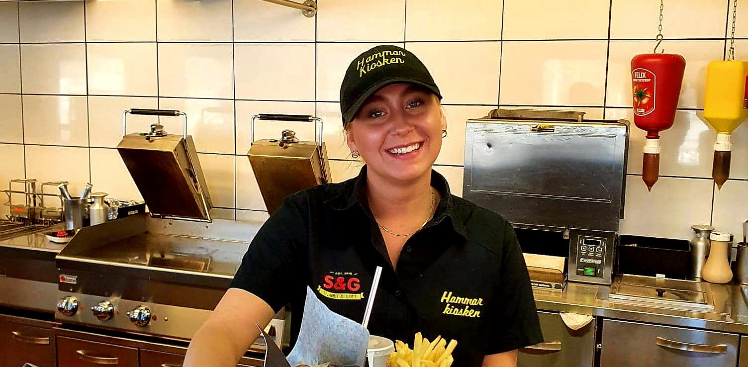 Hammarkioskens personal håller upp en bricka med pommes, dricka och hamburgare.