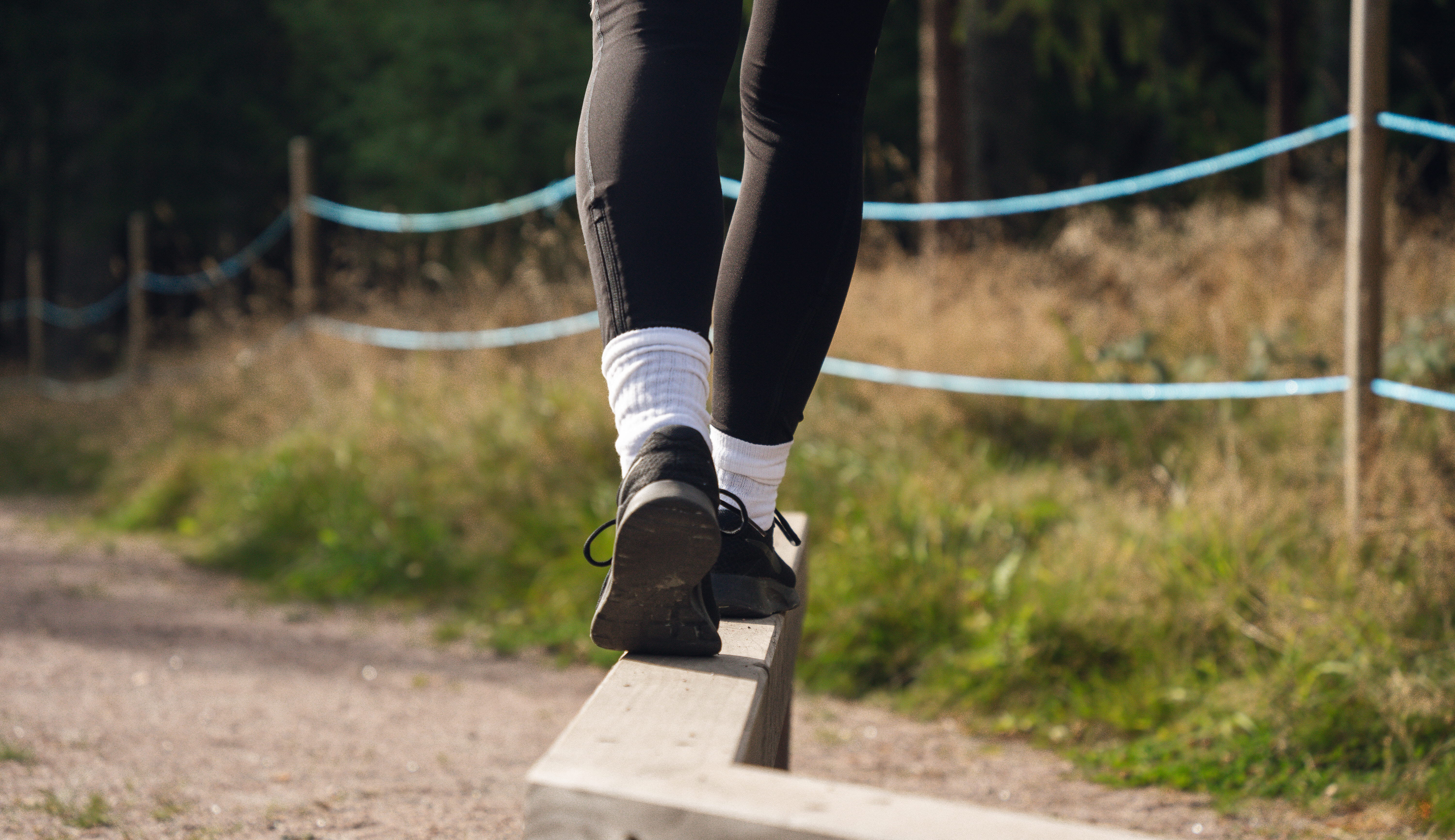 Utegym, en kvinna tränar på en balansgång man ser endast fötter och ben. 