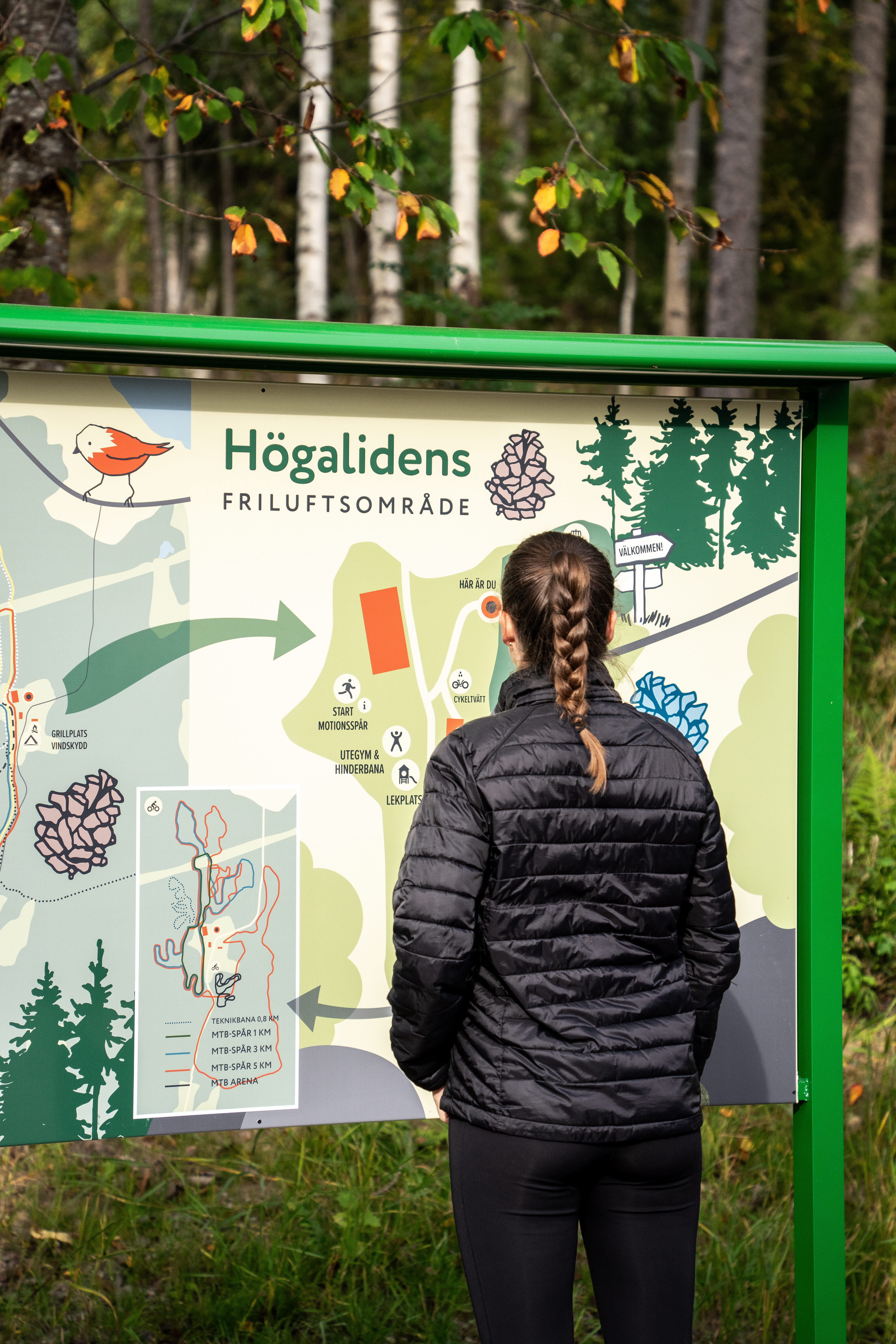 En kvinna som tittar på en skylt med en karta över Högalidens friluftsområde