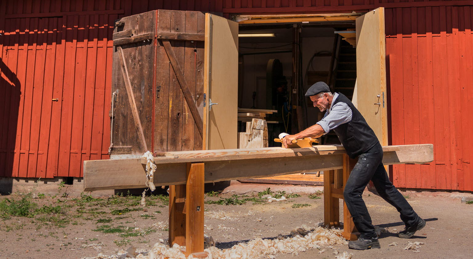 Man som handhyvlar panel framför gamla brandstationen, Stadsgården i Hjo. 