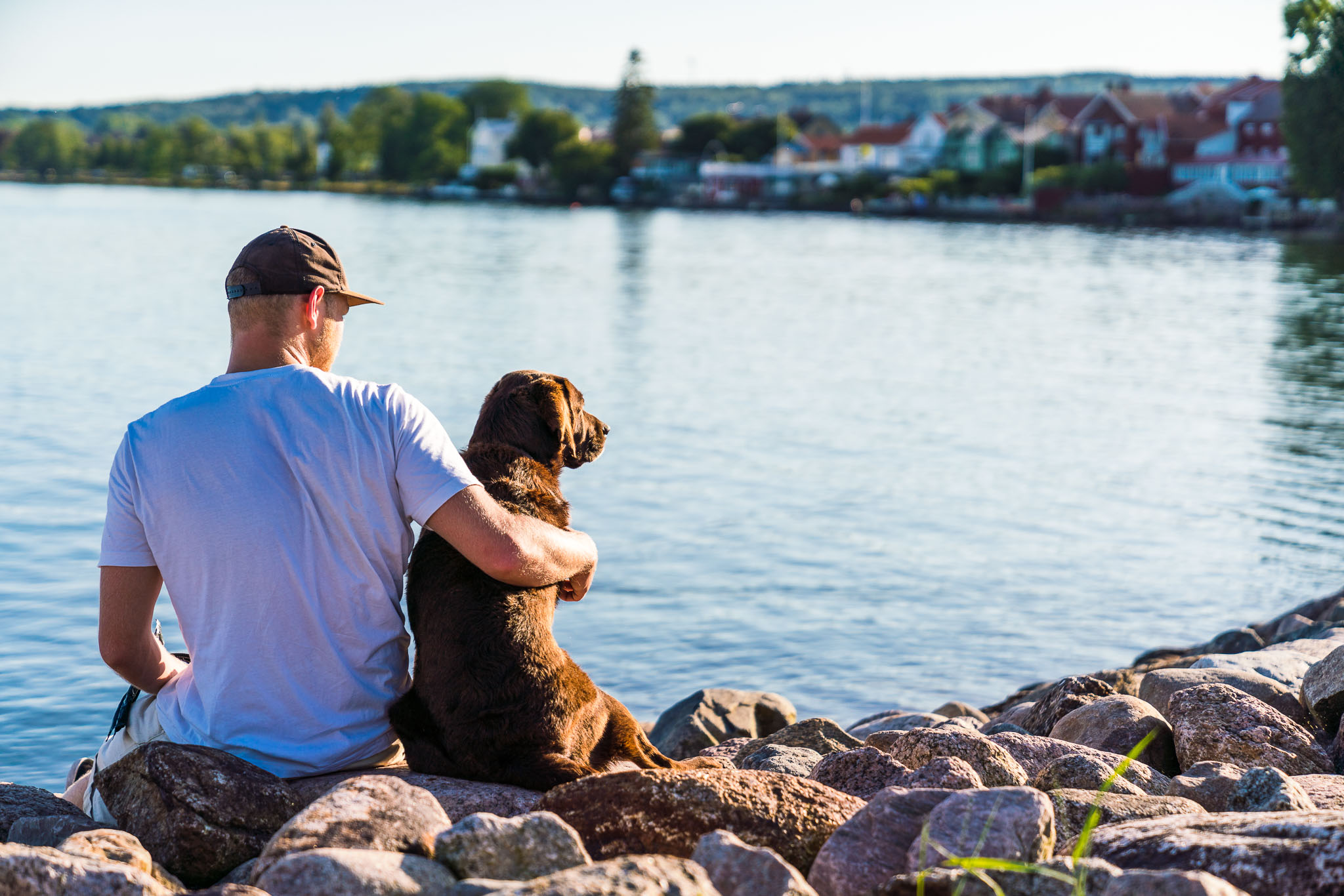 Ung man med hund som sitter i Hjo hamn och tittar ut över Vättern och Hjo stad. 