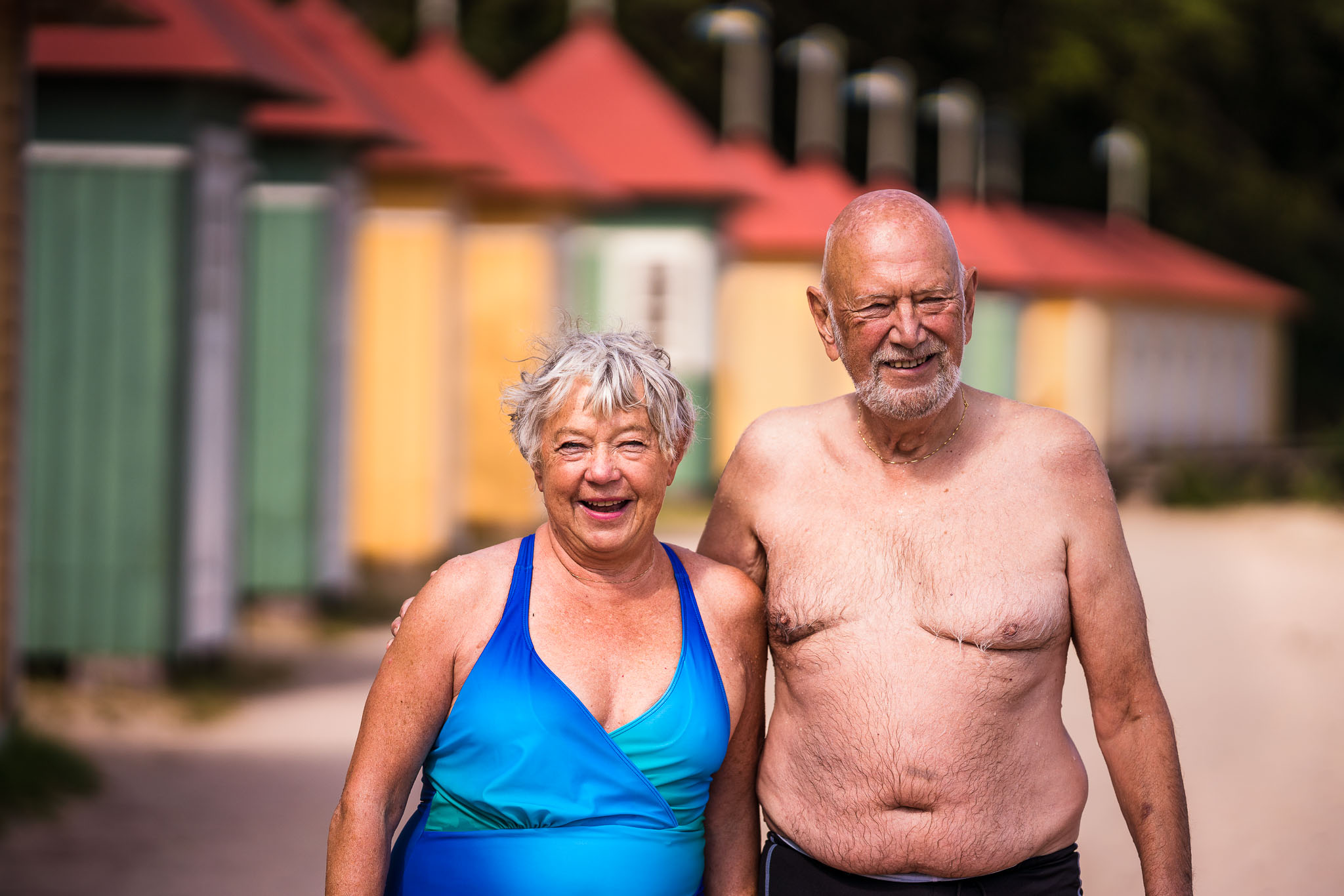 Äldre par vid Guldkroksbadets sandstrand, framför badhytter.