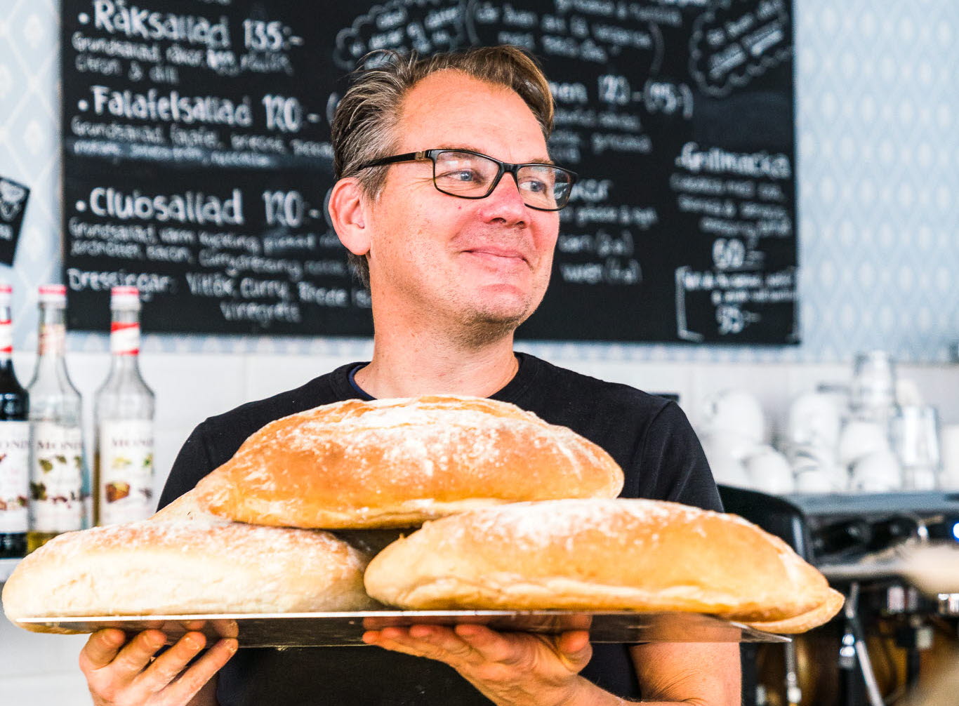 Café owner in his café, with newly baked bread in his hands. 
