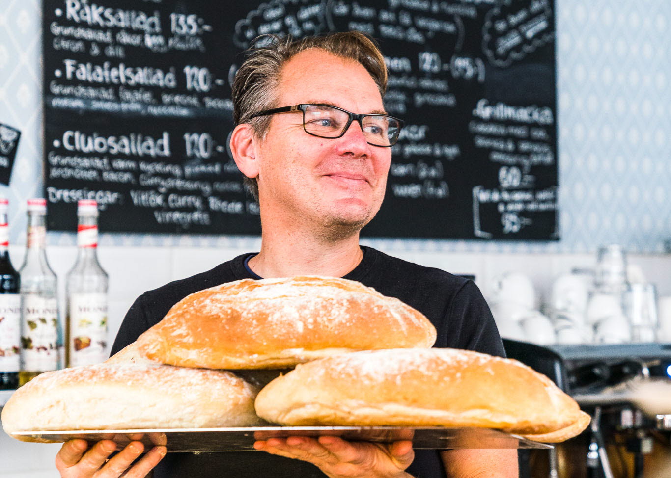 Café owner in his café, with newly baked bread in his hands. 