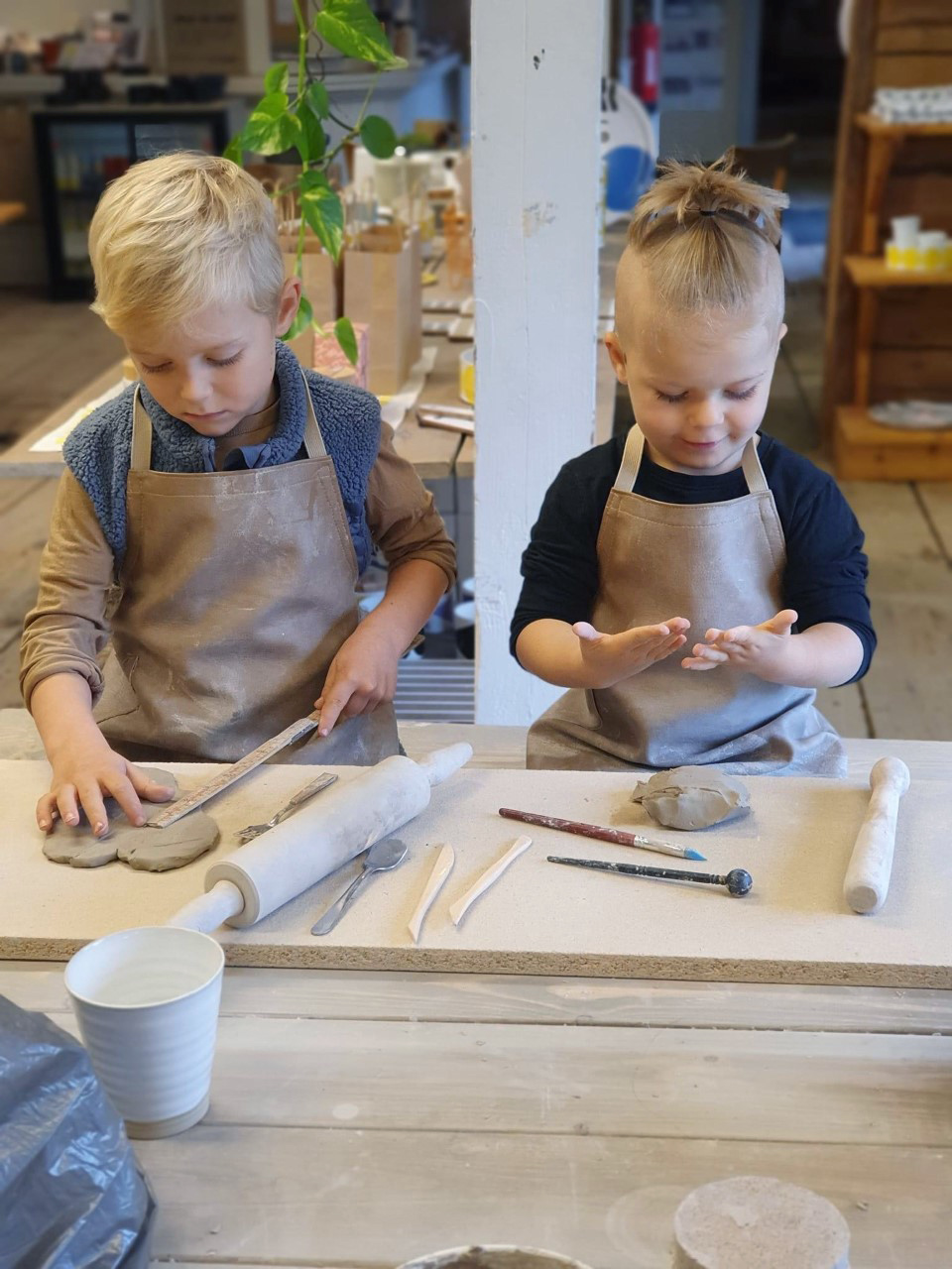 Två barn sitter och leker med lera i en keramikstudio. 