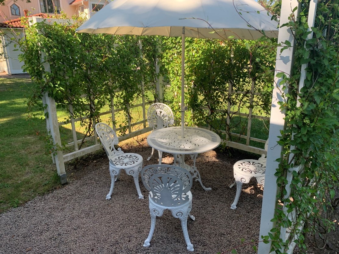 Uteplats med fyra vita stolar och ett vitt bord. Växer grönt runt om platsen. 