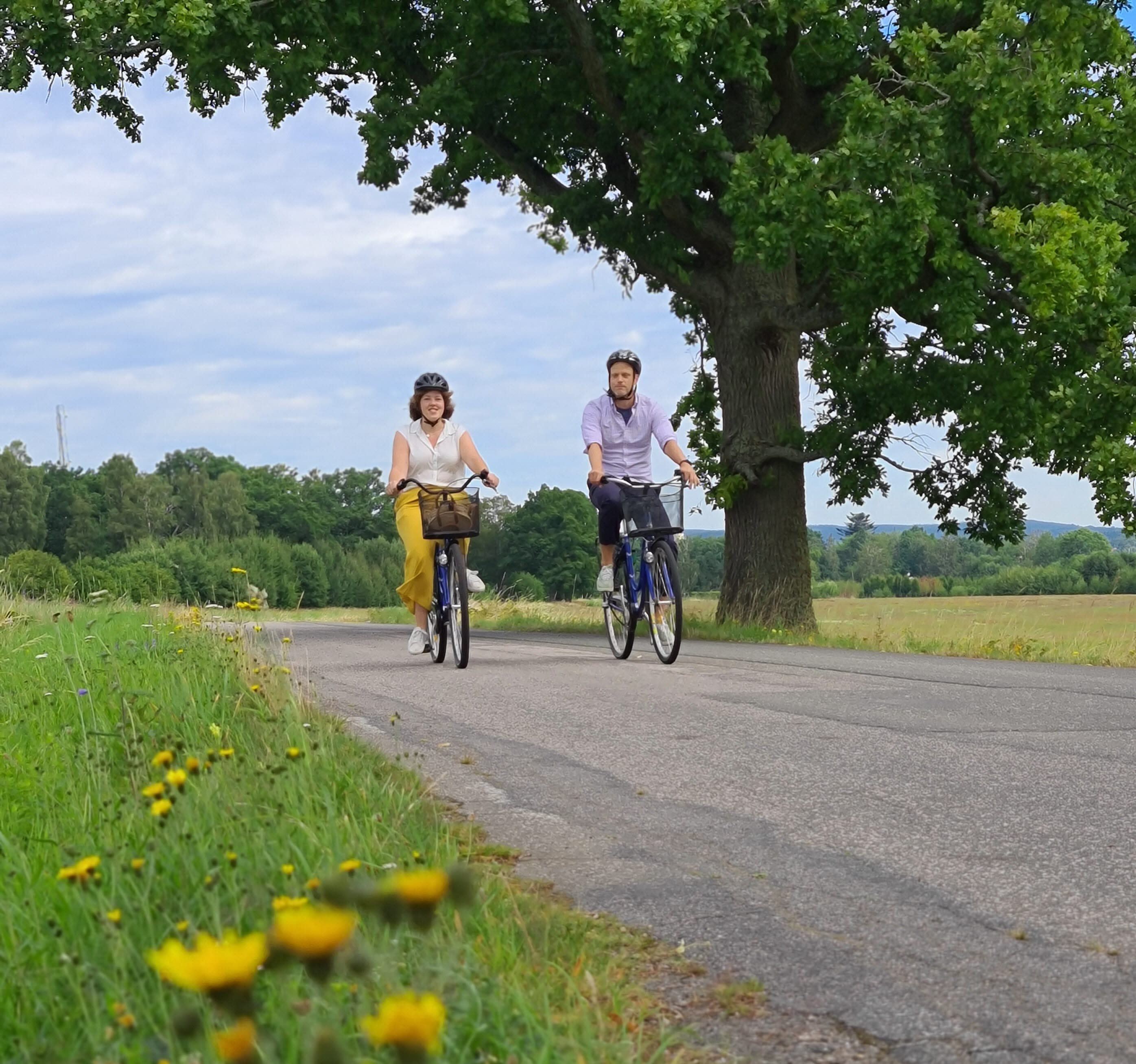 Två personer cyklar på en landsväg en varm sommardag.