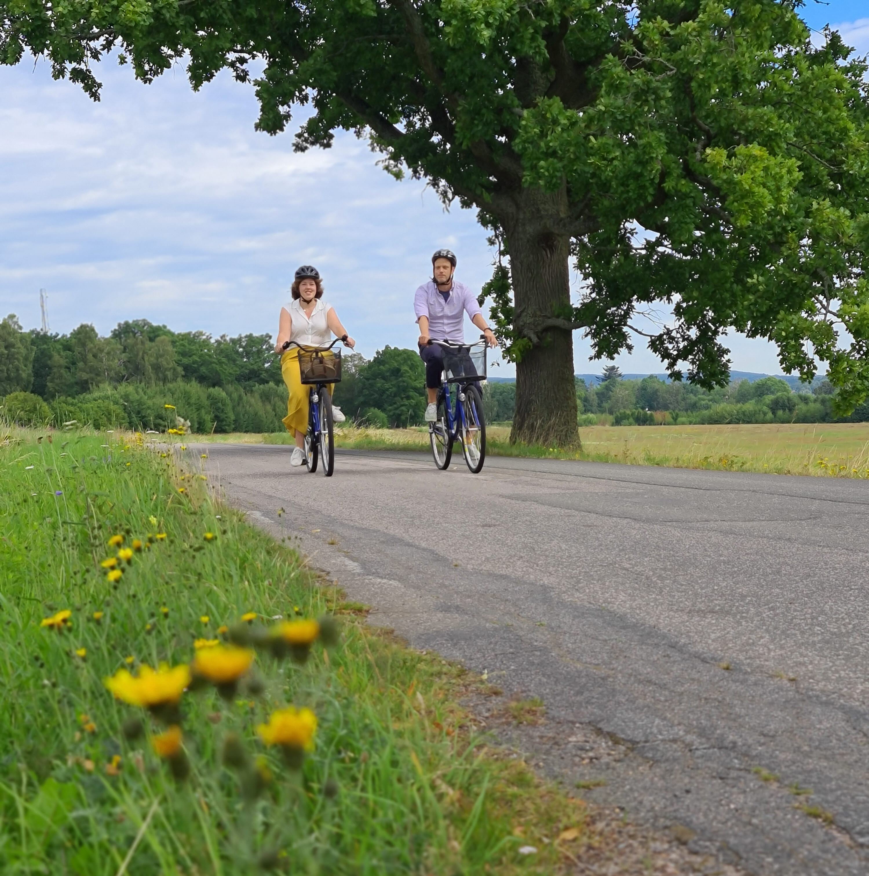 Två personer cyklar på en landsväg en varm sommardag.