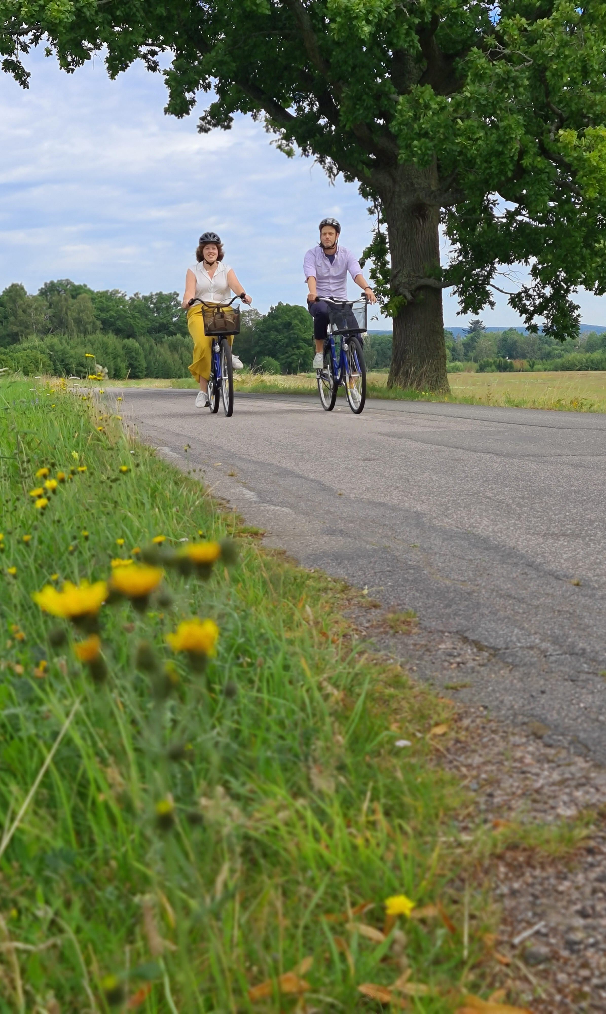 Två personer cyklar på en landsväg en varm sommardag.