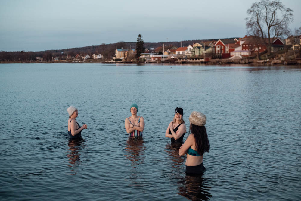Fyra kvinnor står i vattnet med en stad som ligger bakom. 