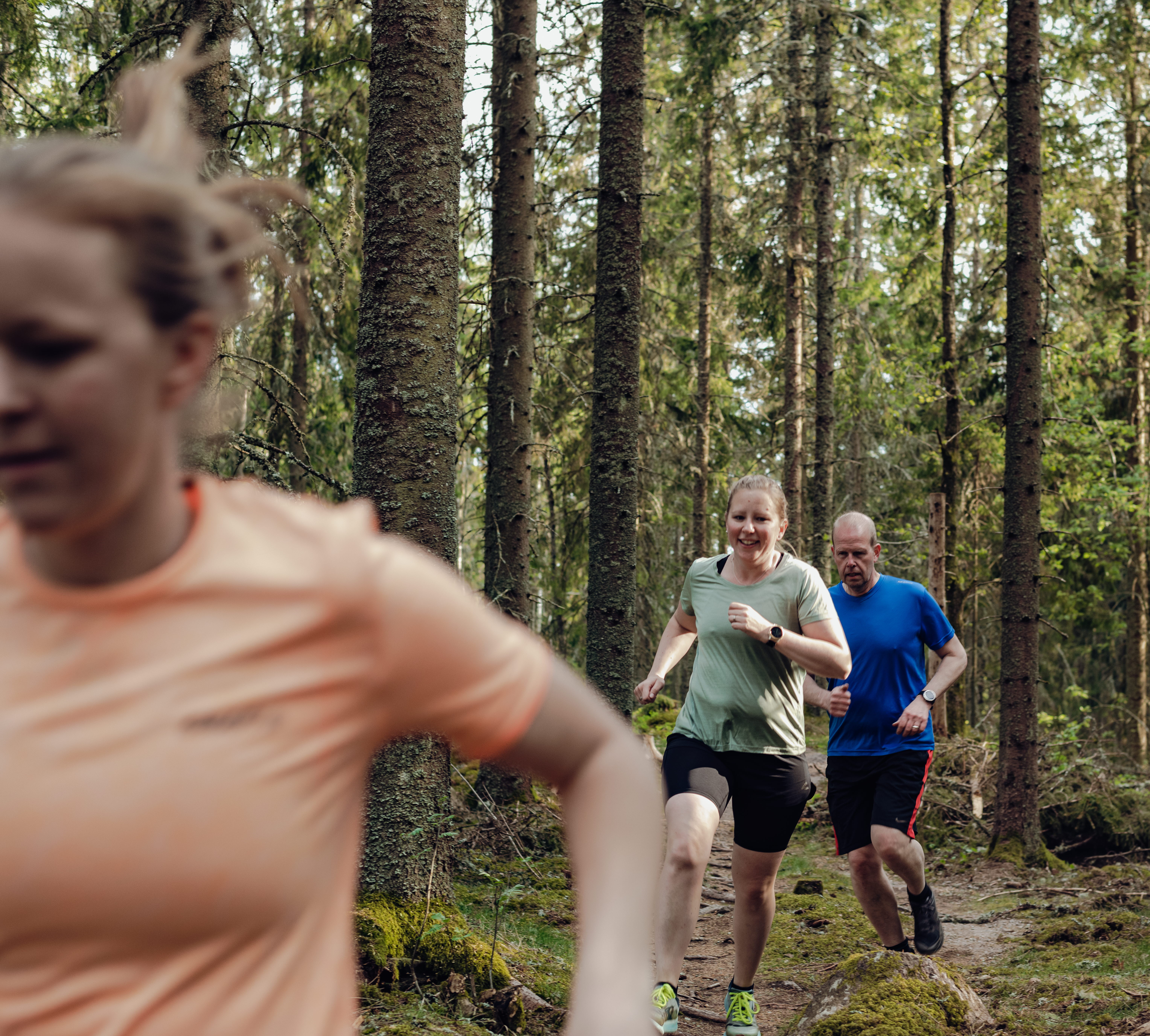 tre personer springer på en mindre stig i skogen. 