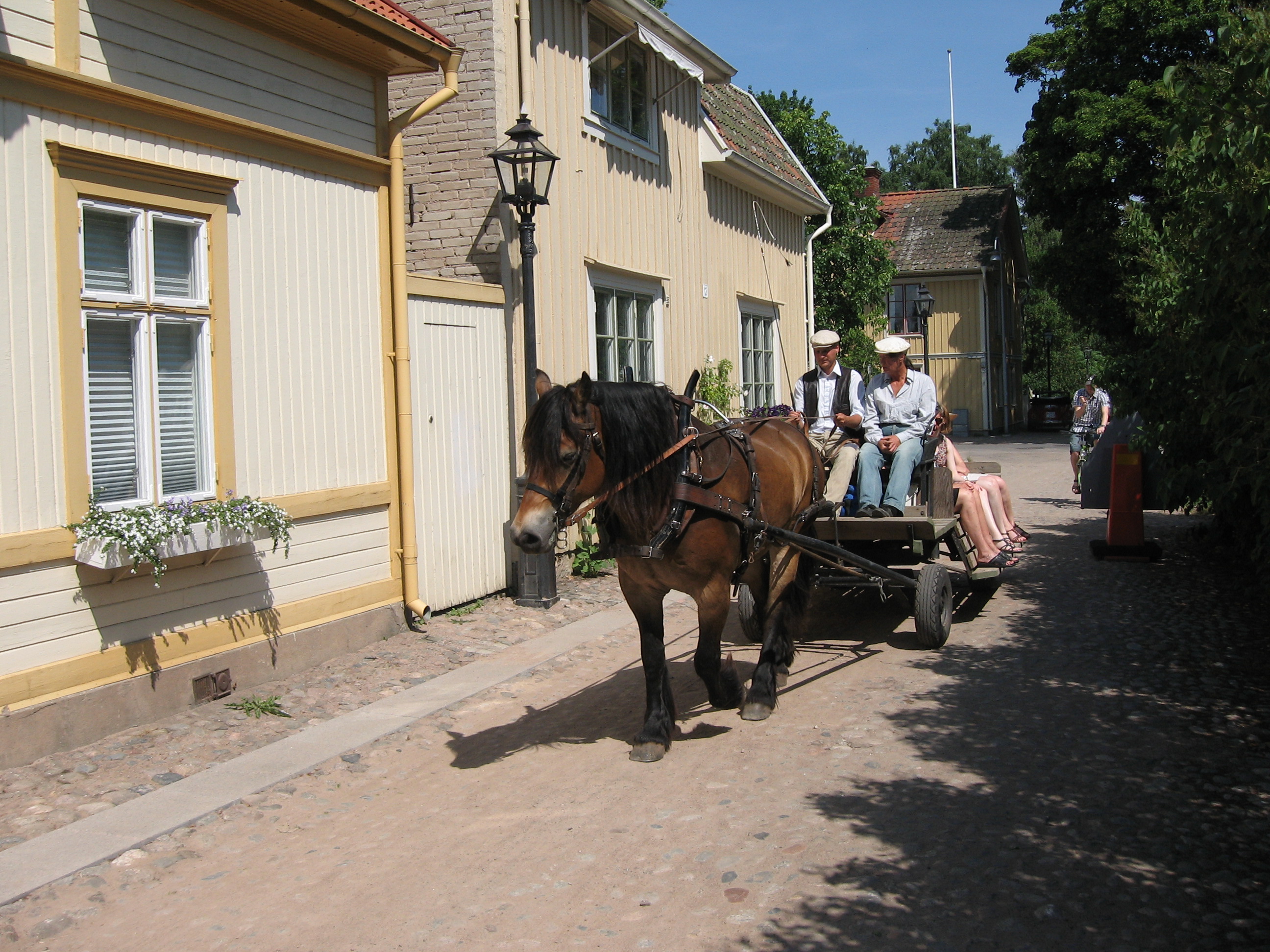 Häst och vagn tar sig genom trästaden Hjo med människor som last.