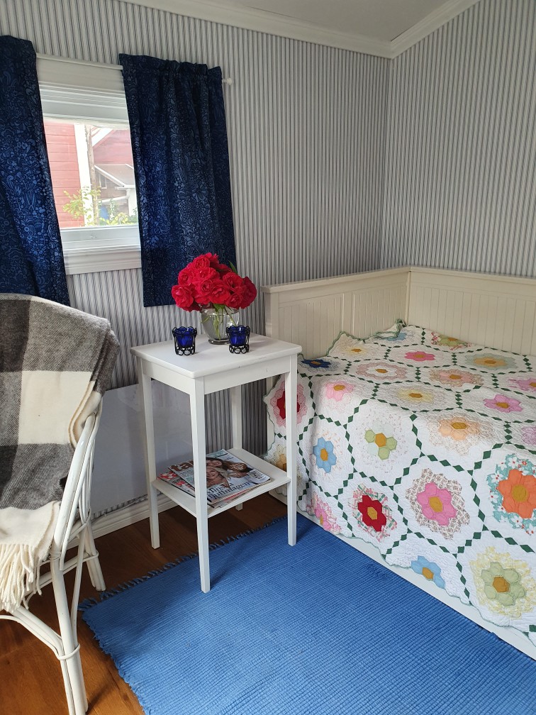 interiörbild med ett litet fönster, en säng med sängbord och en fåtälj. 