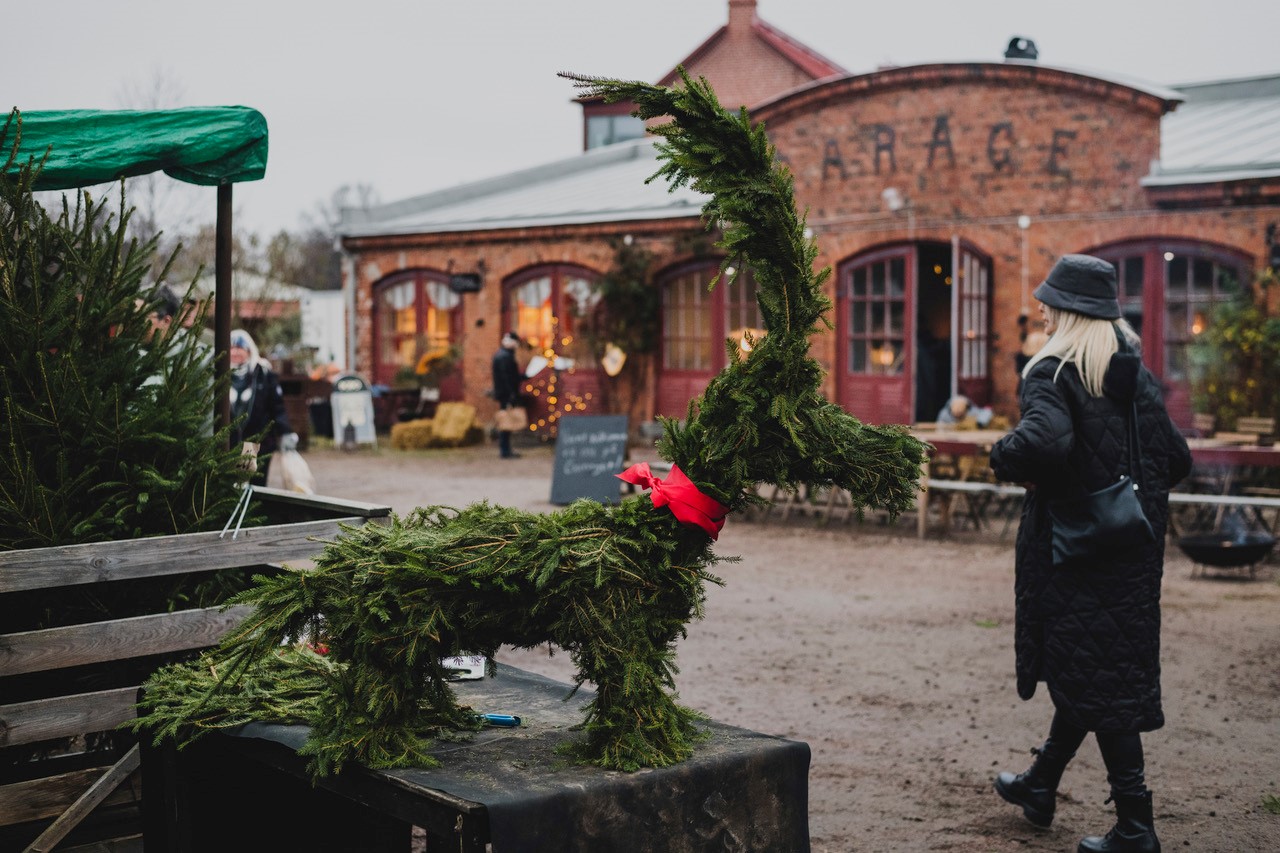 En kvinna i svart jacka går mot en röd tegelbyggnad. det är julmarknad. 