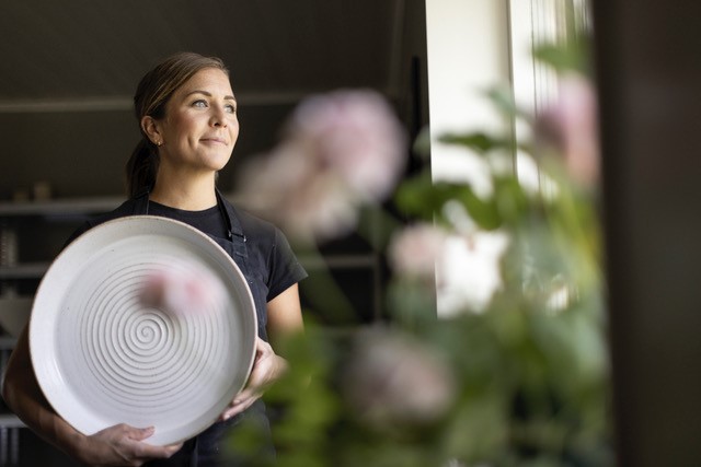 En kvinna står vid ett fönster och håller ett stort keramikfat