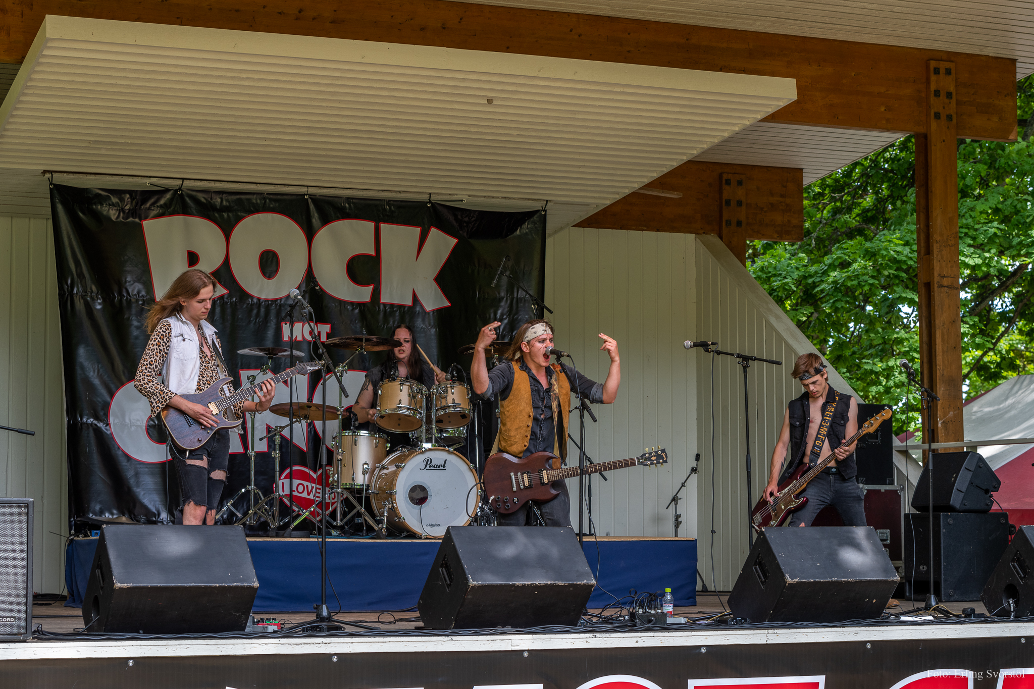 Fyra personer står på en scen med instrument och en sjunger med händerna i luften