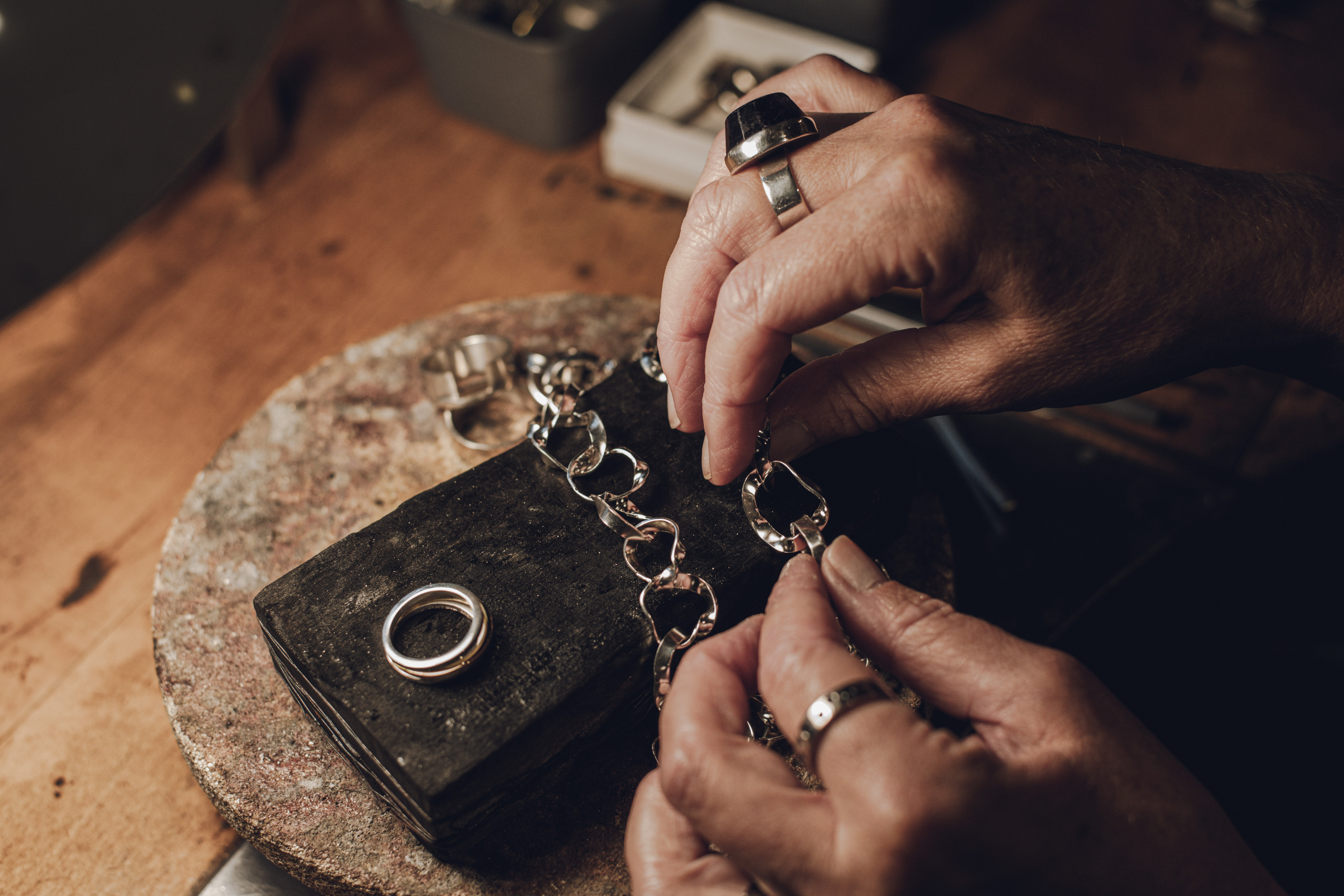 Två händer pysslar med ett smycke. Man ser en ring bredvid. 