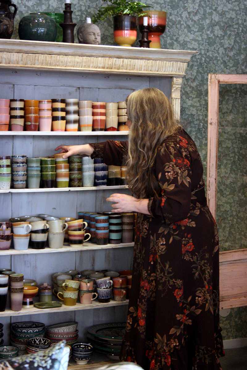 Marie justerar bland keramikmuggar i en hylla