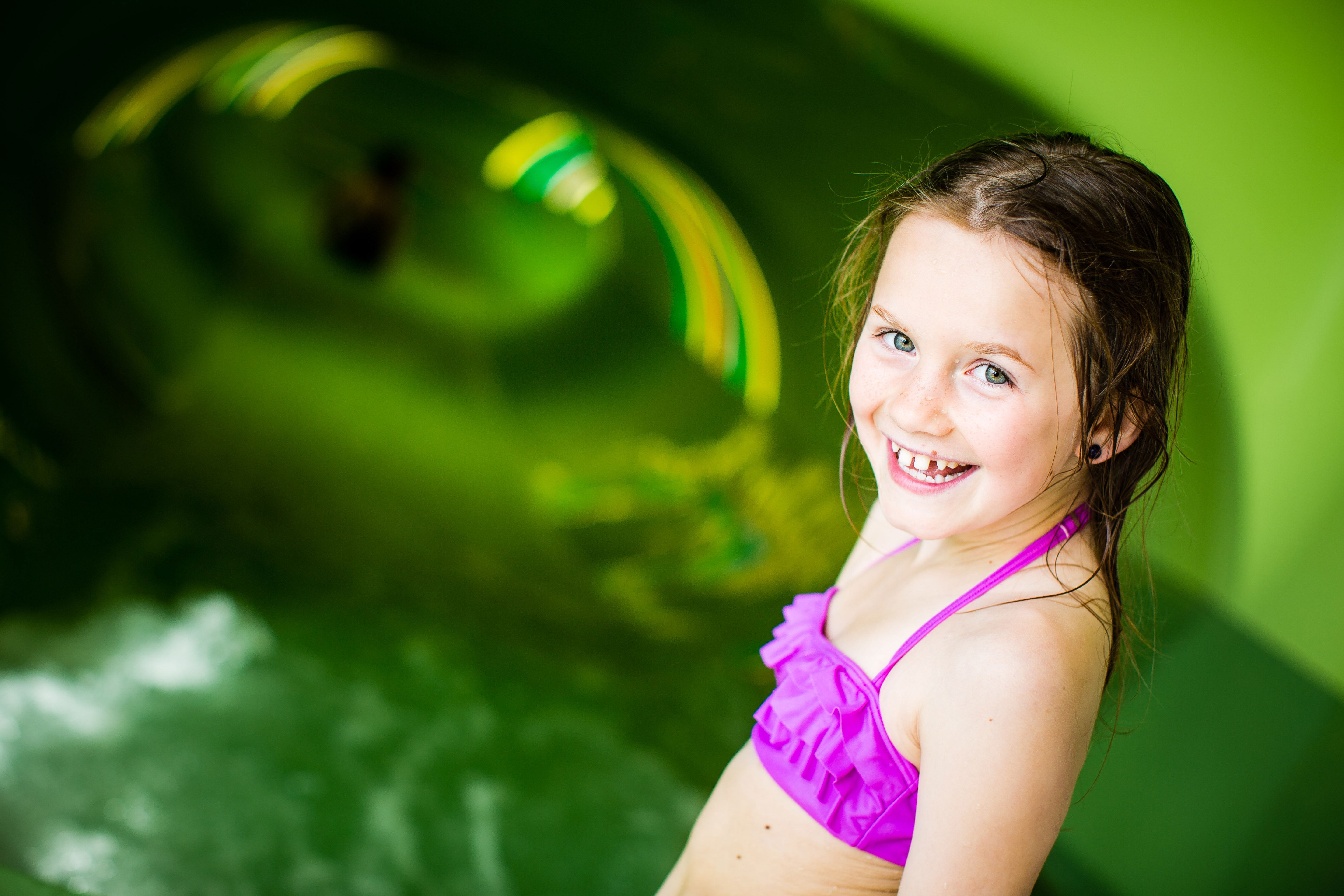Tjej med rosa bikini står i en grön vattenrutschbana. 