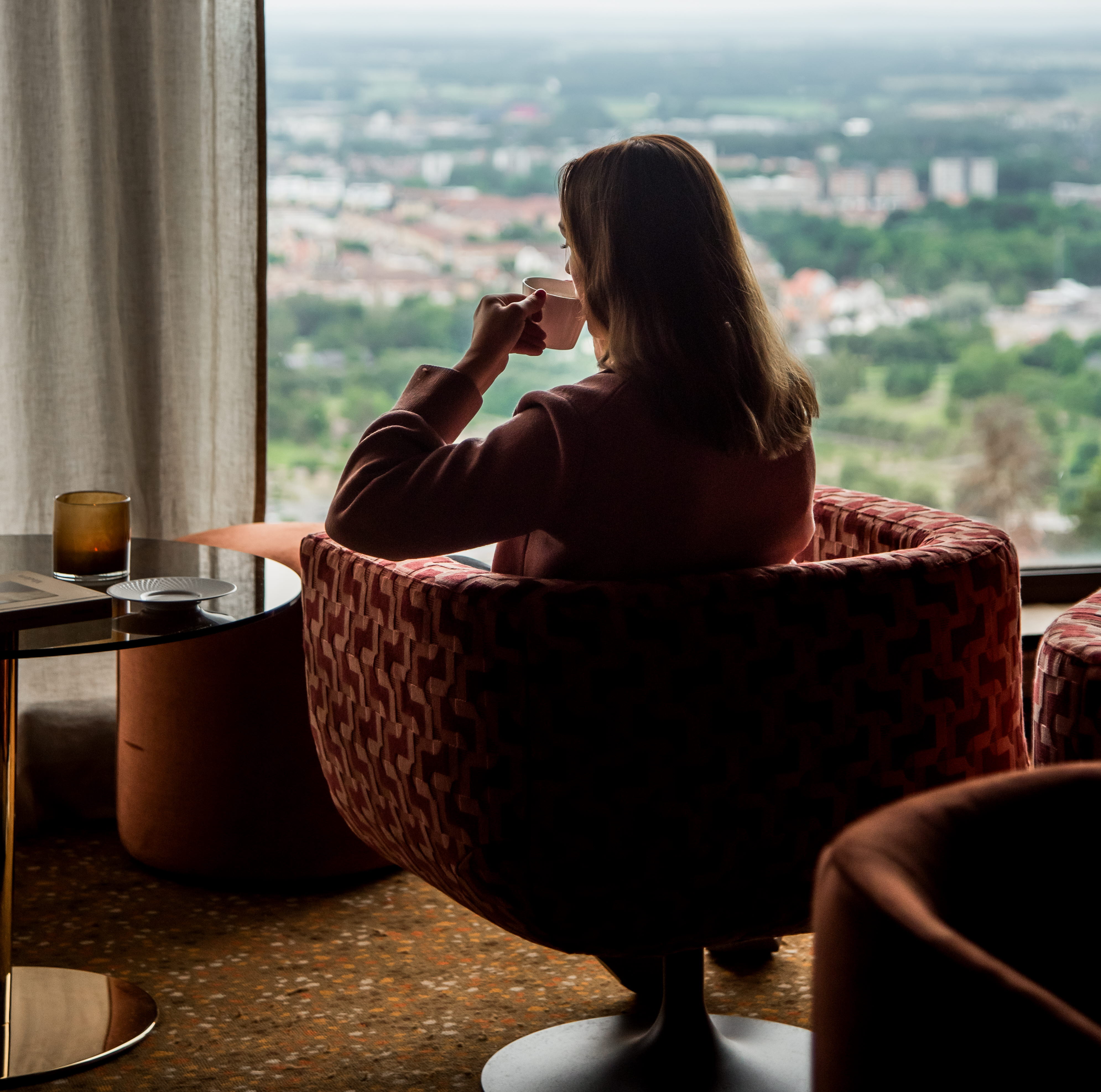 Kvinna som sitter i en fåtölj och kikar ut genom ett fönster.