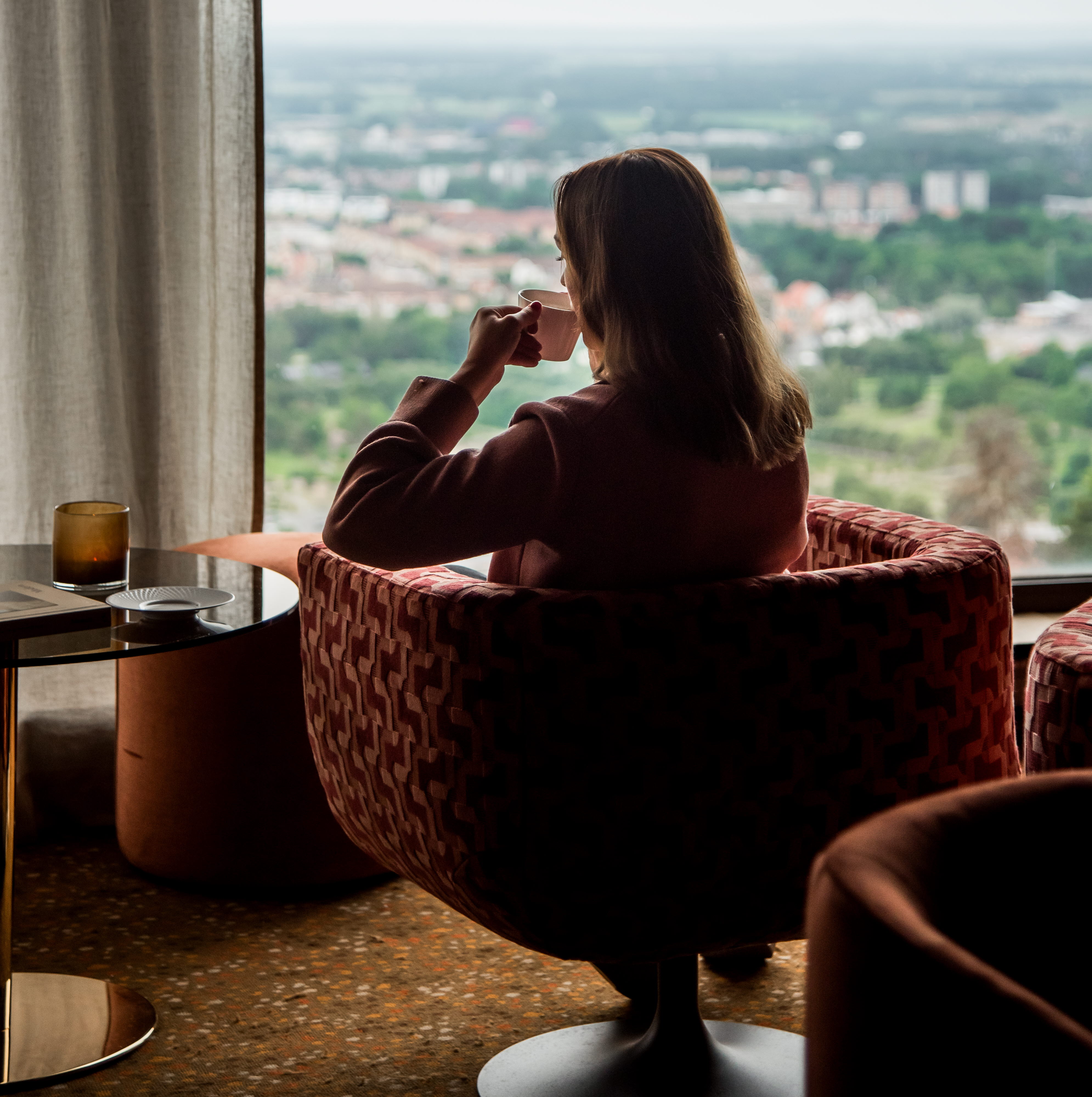 Kvinna som sitter i en fåtölj och kikar ut genom ett fönster.