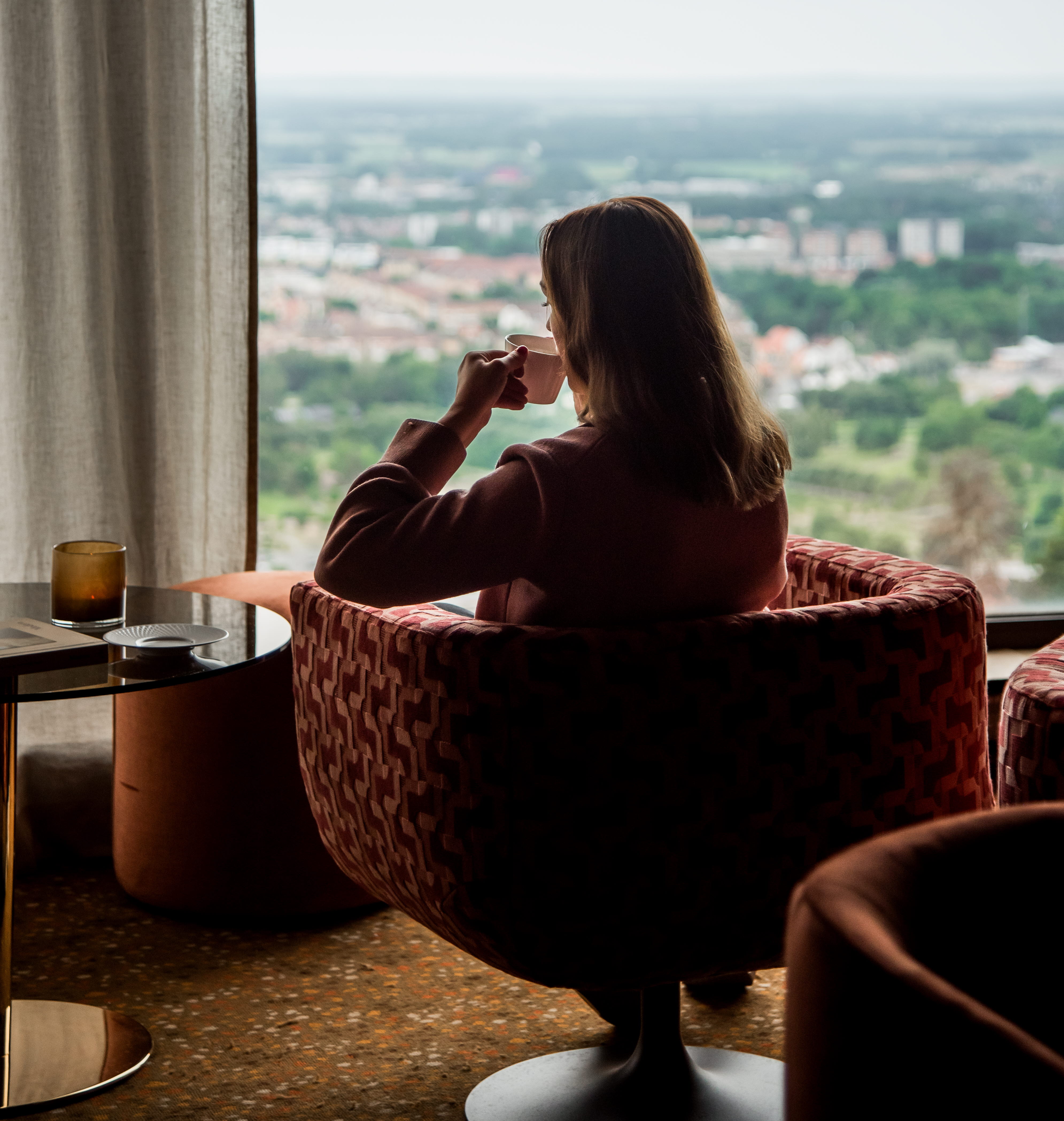 Kvinna som sitter i en fåtölj och kikar ut genom ett fönster.