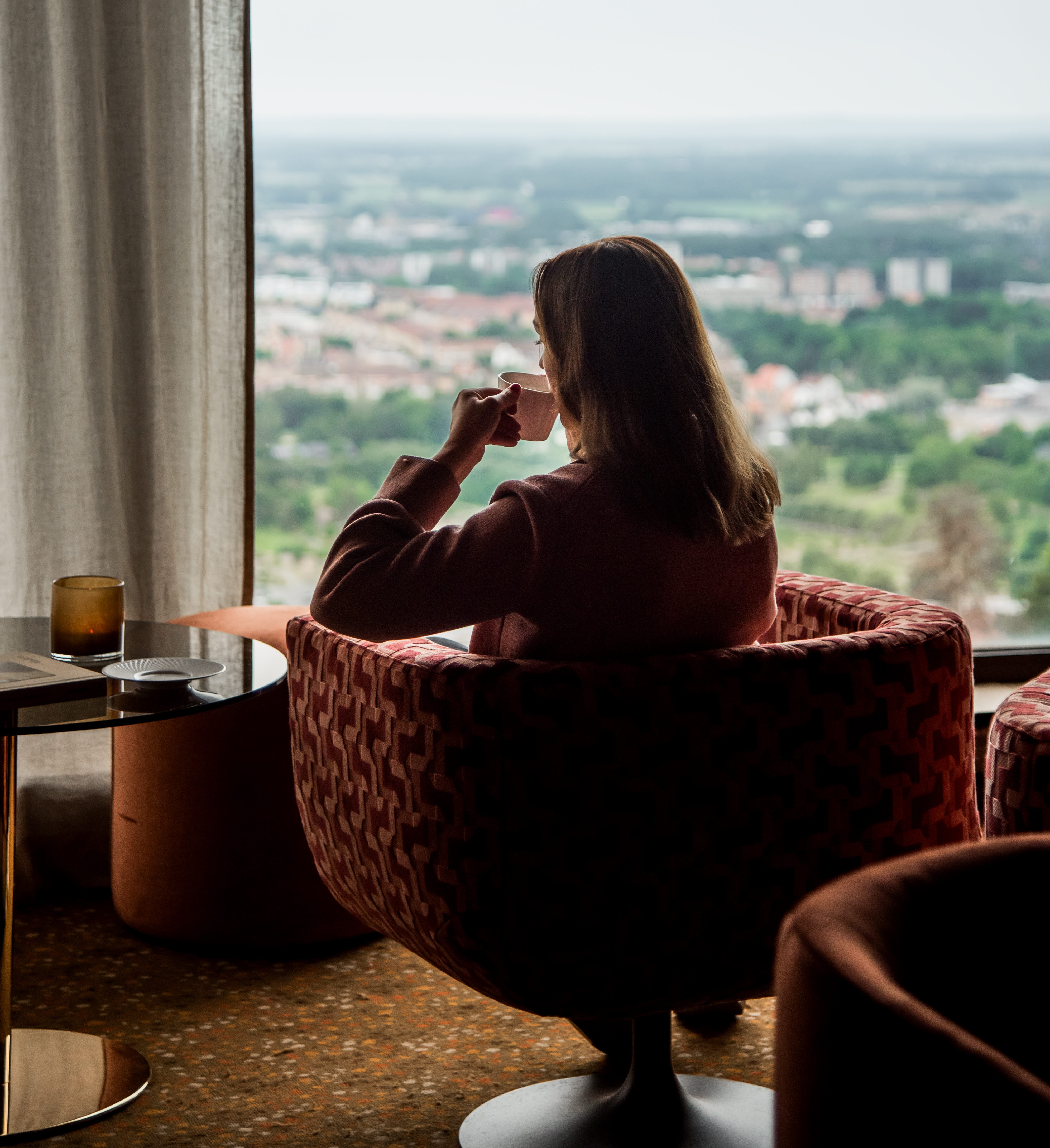 Kvinna som sitter i en fåtölj och kikar ut genom ett fönster.